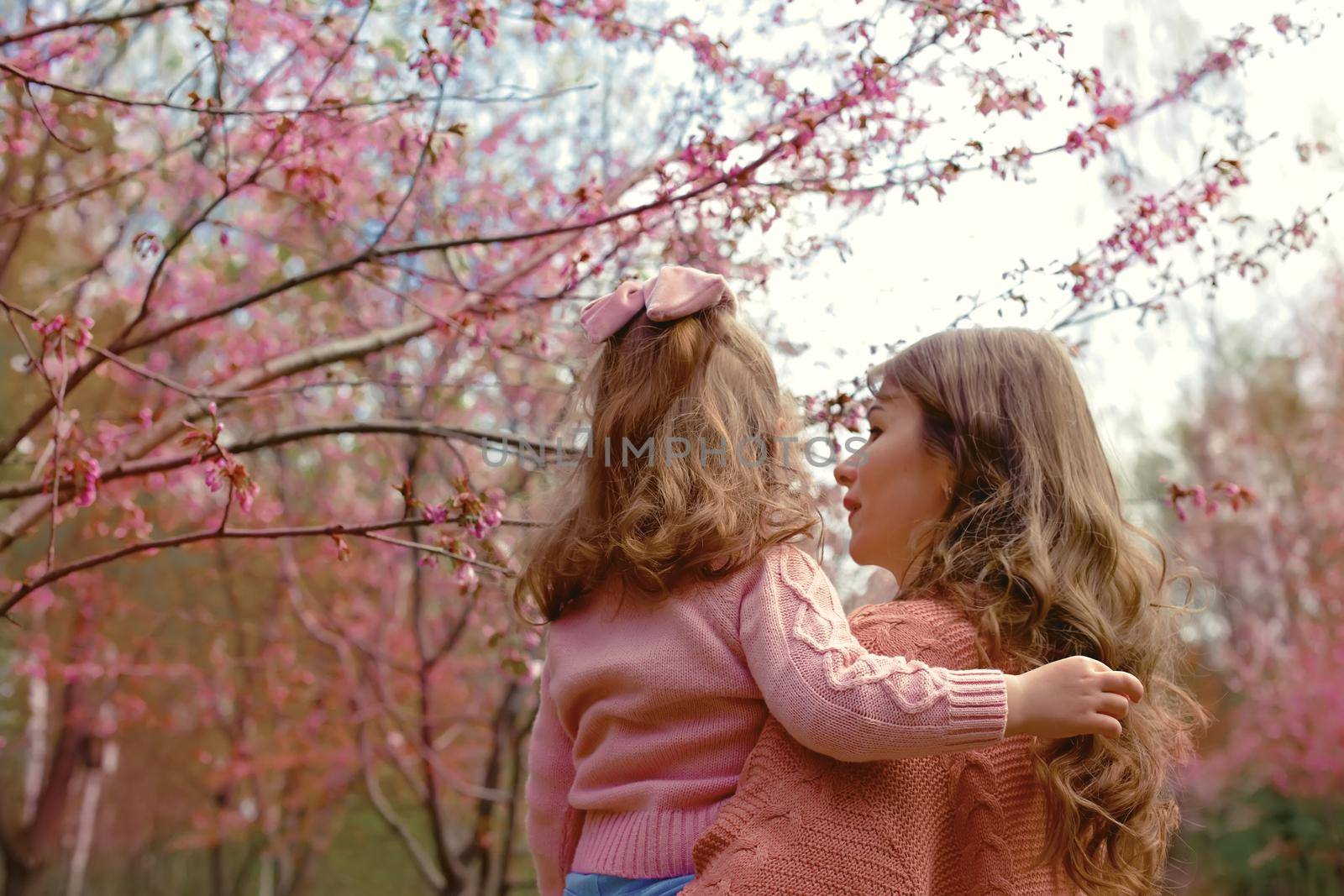 Mother and little daughter, standing in the park under a flowering cherry tree. Back view. copy space