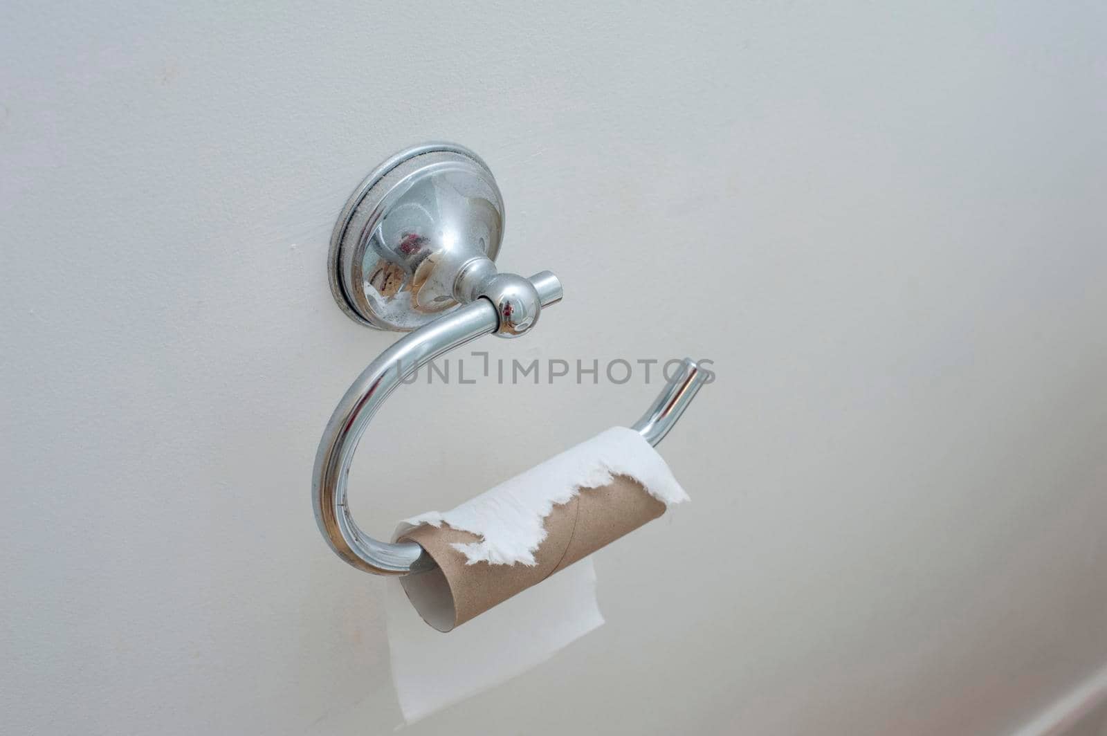 Toilet paper holder on white wall with an empty roll of paper