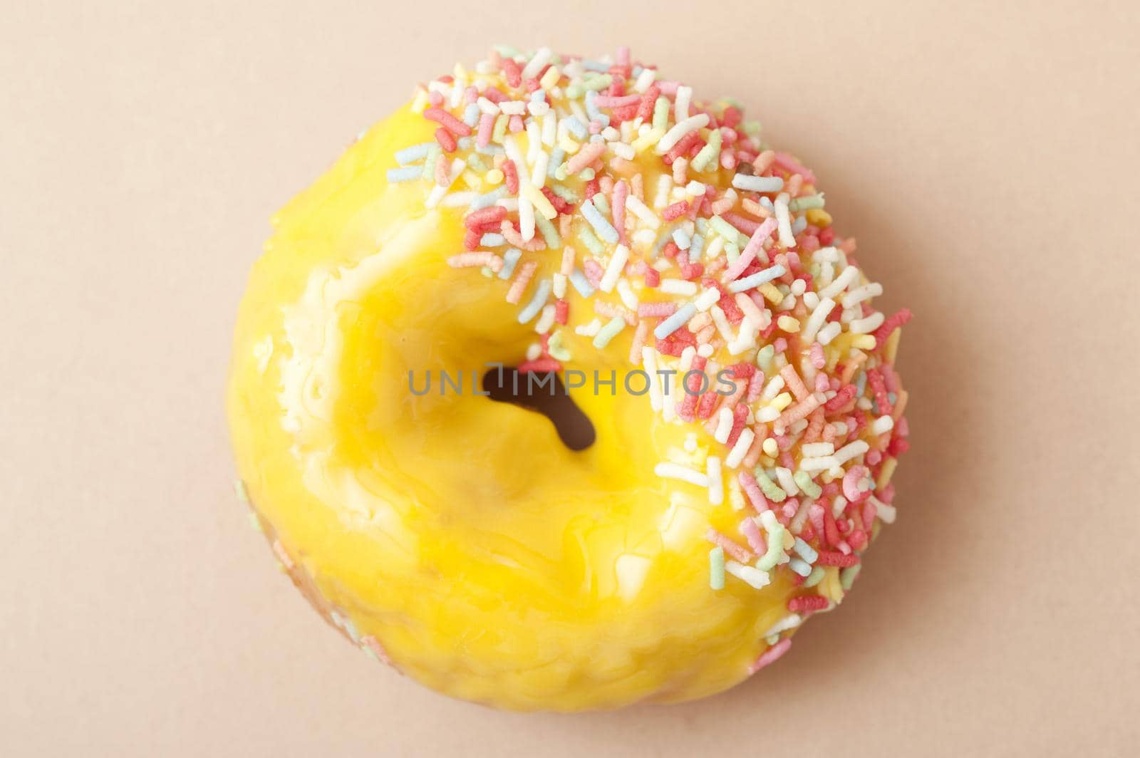 Glazed lemon ring doughnut with colorful citrus icing dipped in multicolored sprinkles on one side, overhead view on a neutral background