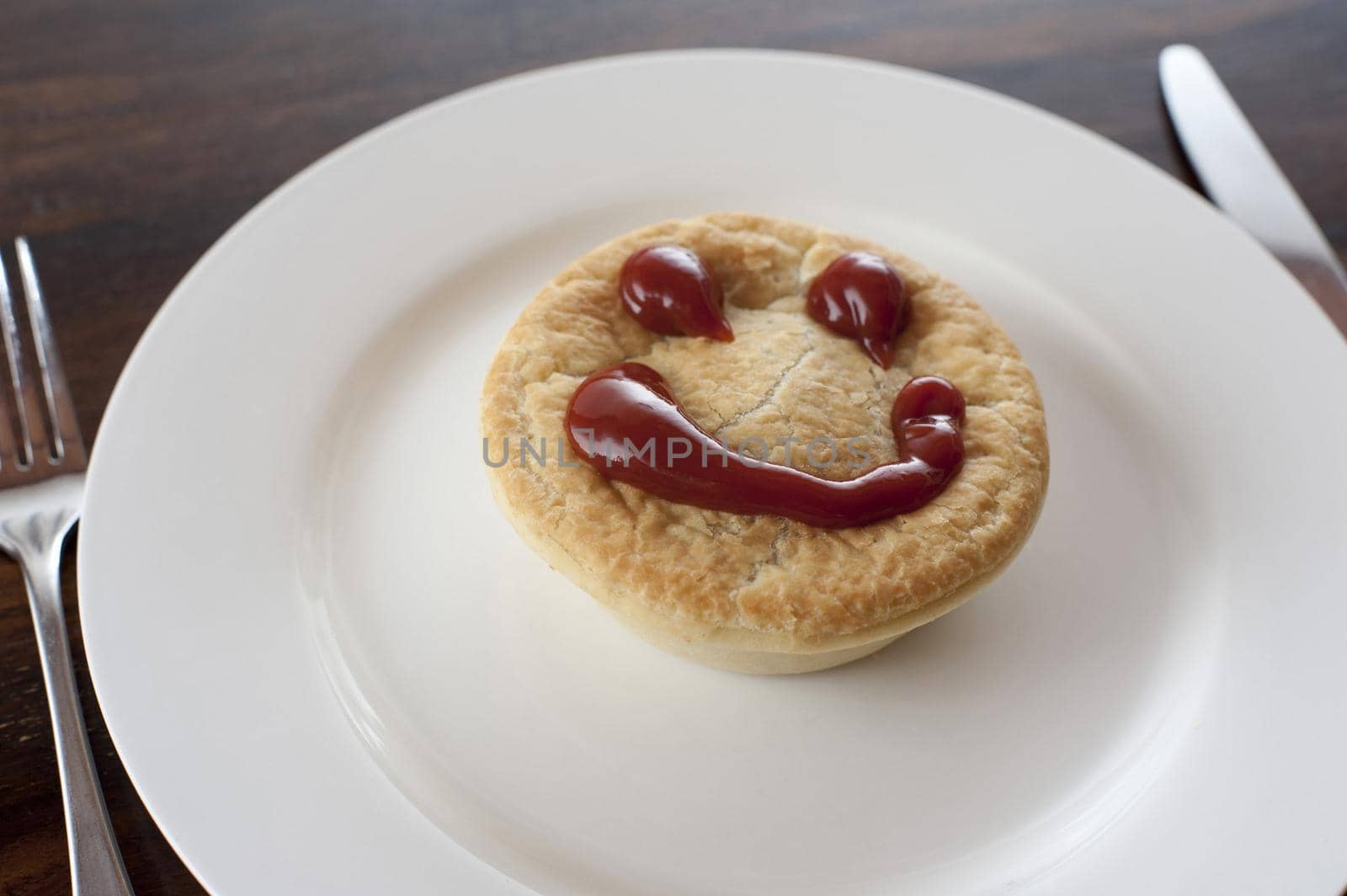 Meat pie with a happy face made of tasty sauce on top of the pastry crust served on a plain white plate