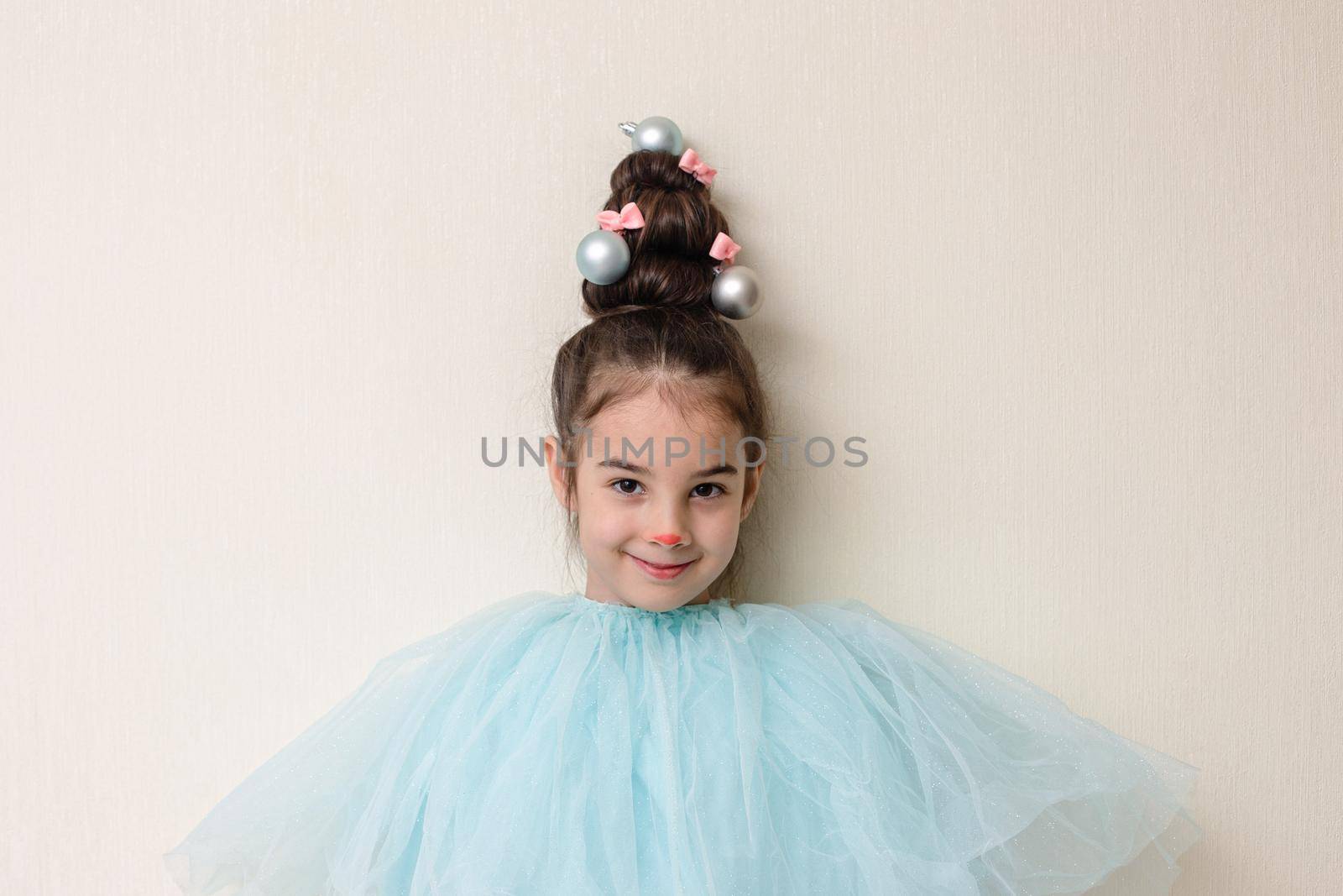 Portrait of funny beautiful girl with a hairstyle in the form of a Christmas tree , in blue clothes , stands against the background of a light wall