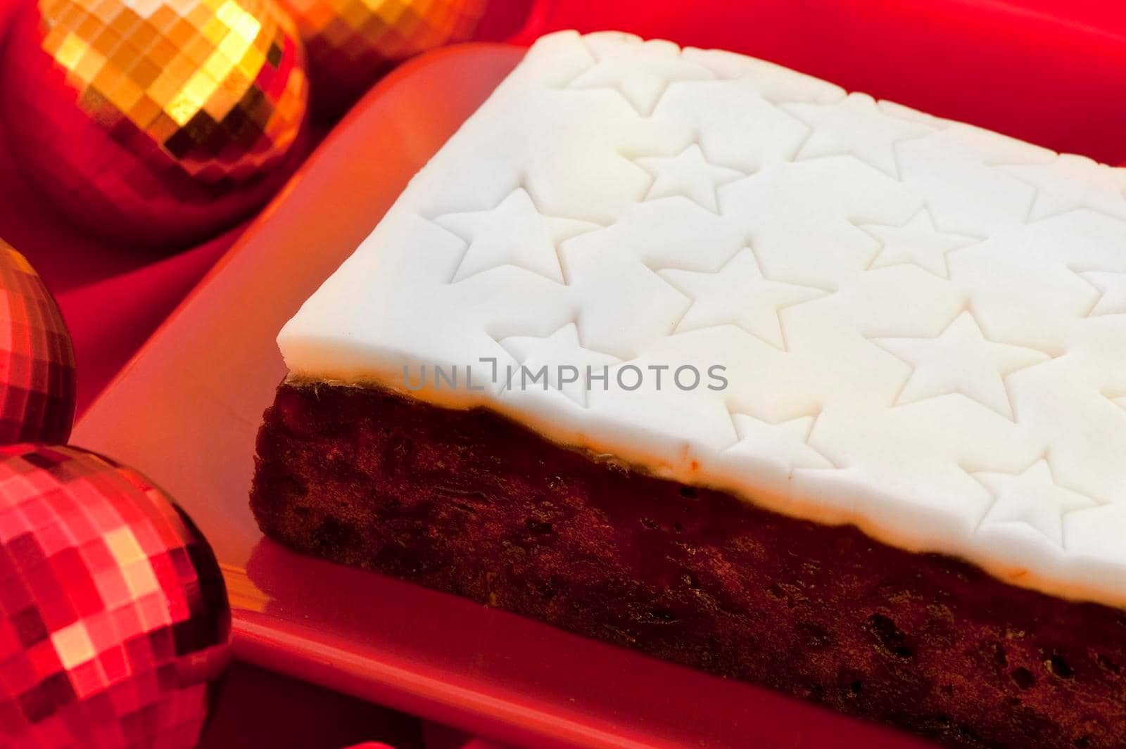 Uncut commercial Christmas fruit cake with a decorative white icing impressed with a pattern of stars on a platter on a festive Christmas table