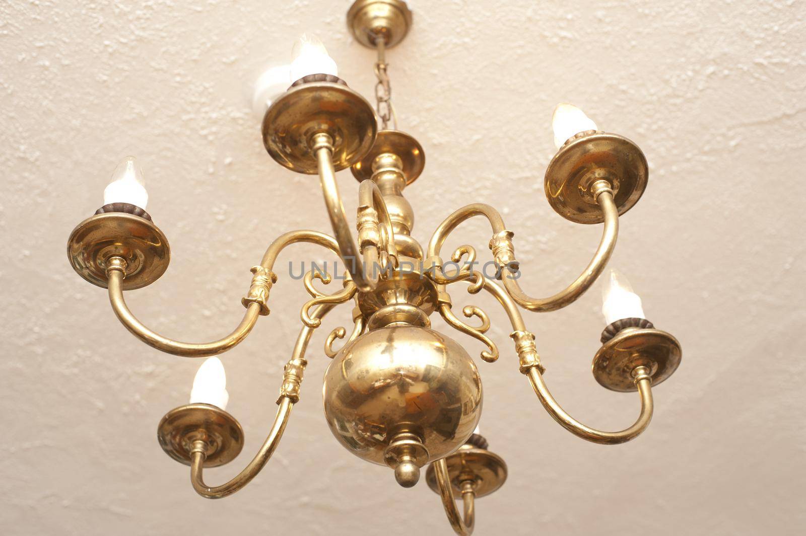 Brass ceiling chandelier with classical candle-style arms viewed from below in an interior decor concept
