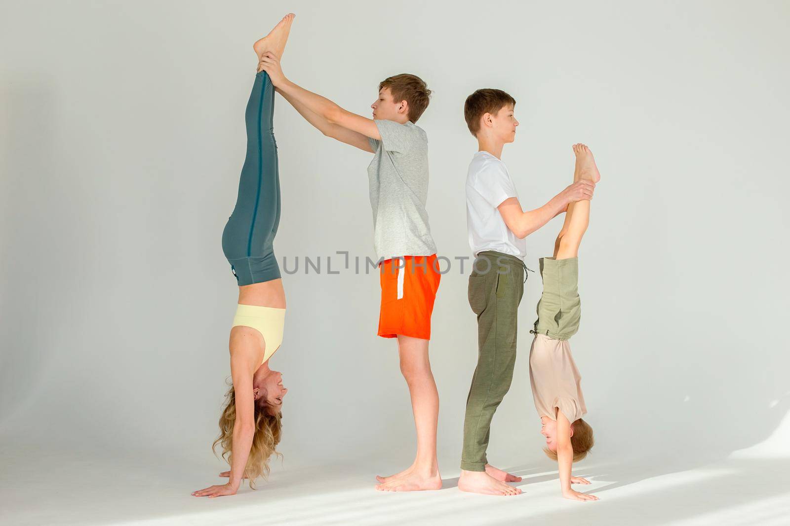 A sports family, a slender woman, a boy and two teenagers stand on their hands, stretching their legs up, perform exercises with support. copy space