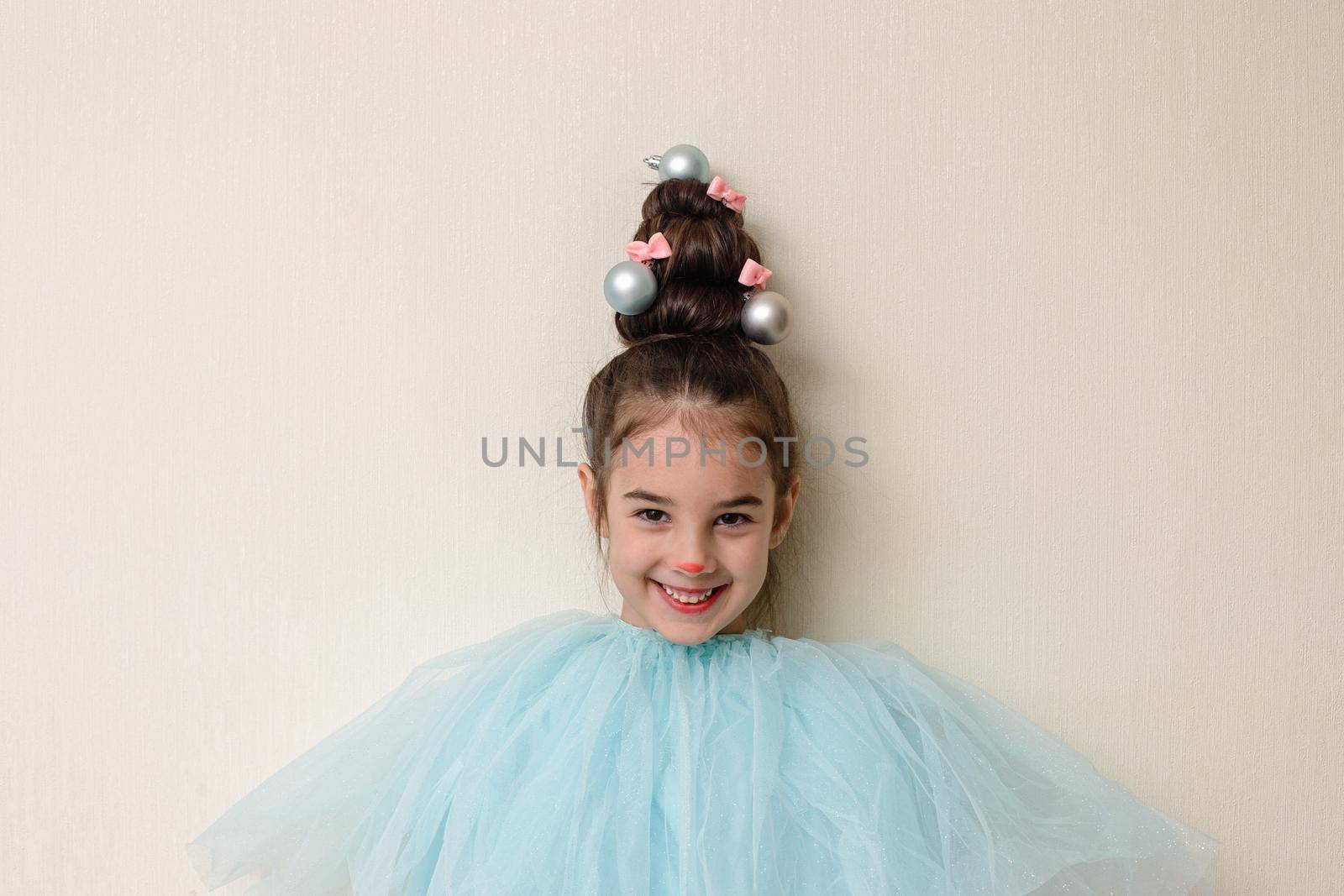 Portrait of funny beautiful girl with a hairstyle in the form of a Christmas tree , stands against the background of a light wall