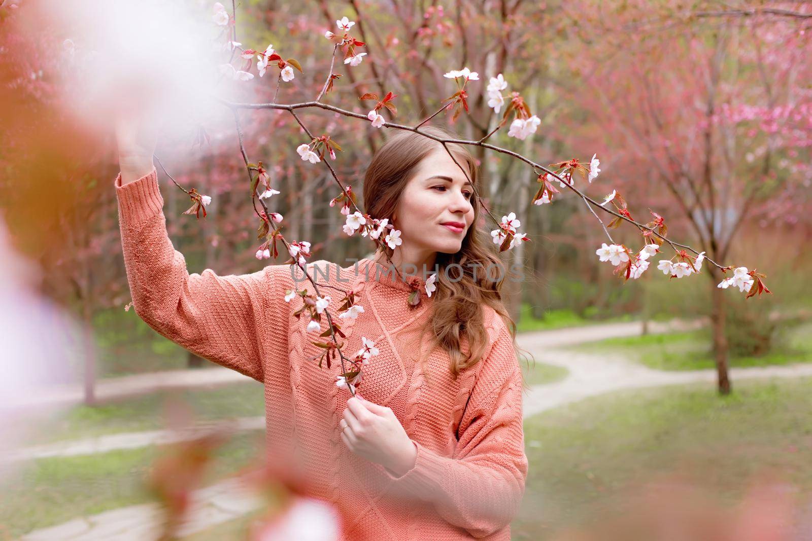 a woman standing under a pink blossoming sakura branch looks away. copy space