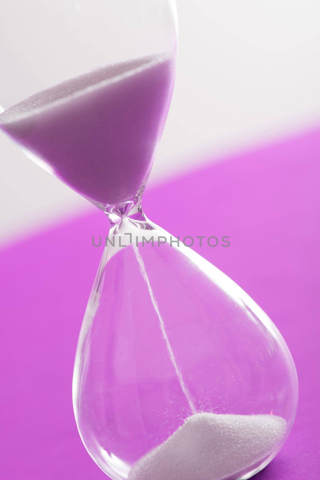 Sand running through an hourglass measuring the passing time counting down to a deadline over a bright pink background