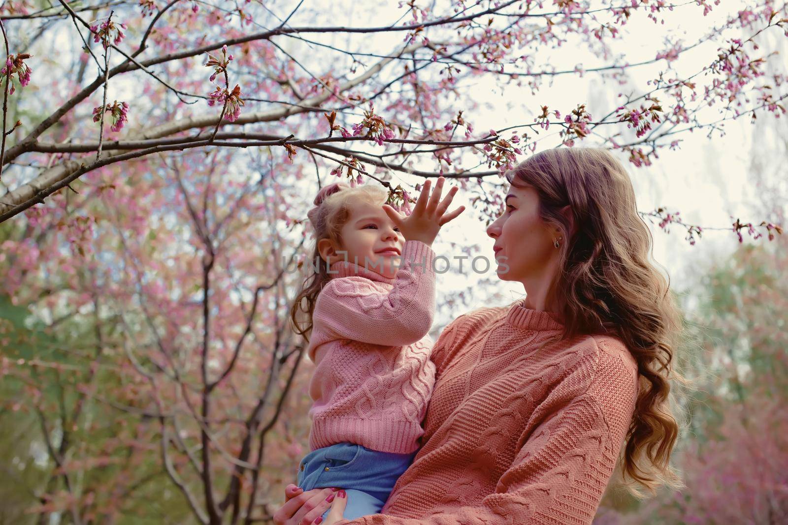 Mother and little daughter, standing in the park under a blossom tree by Zakharova