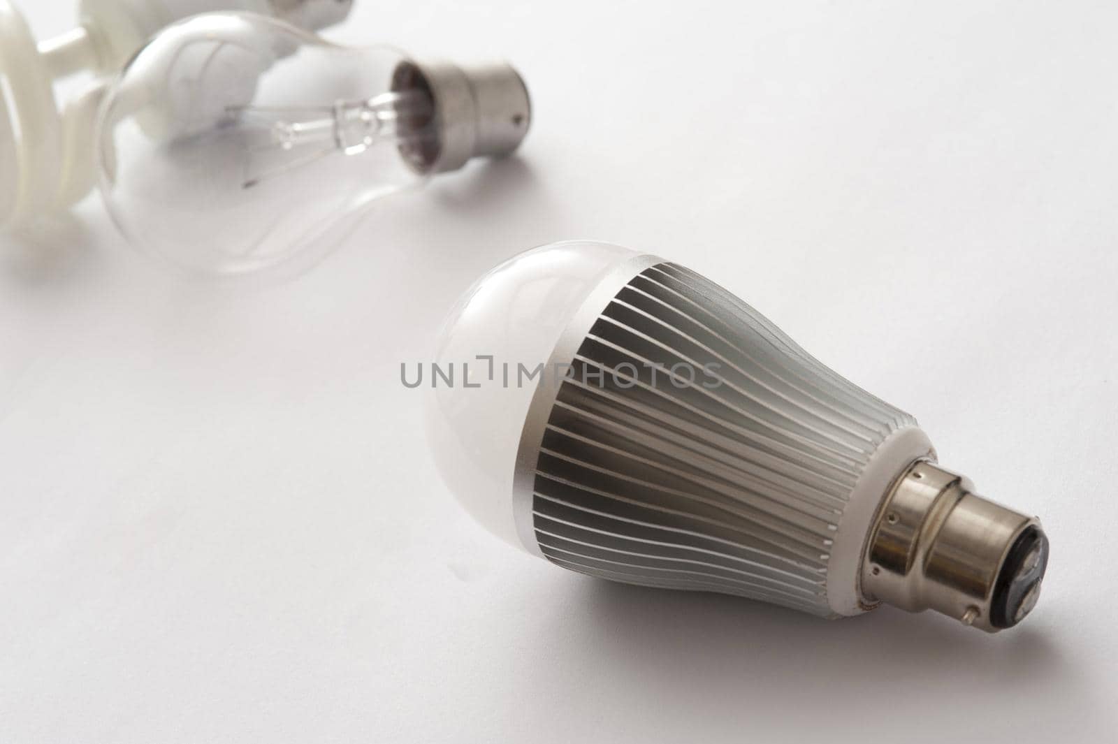 heatsink on a bayonet cap LED energy efficient light bulb, with older incandescent lamp and CF lamp in the background