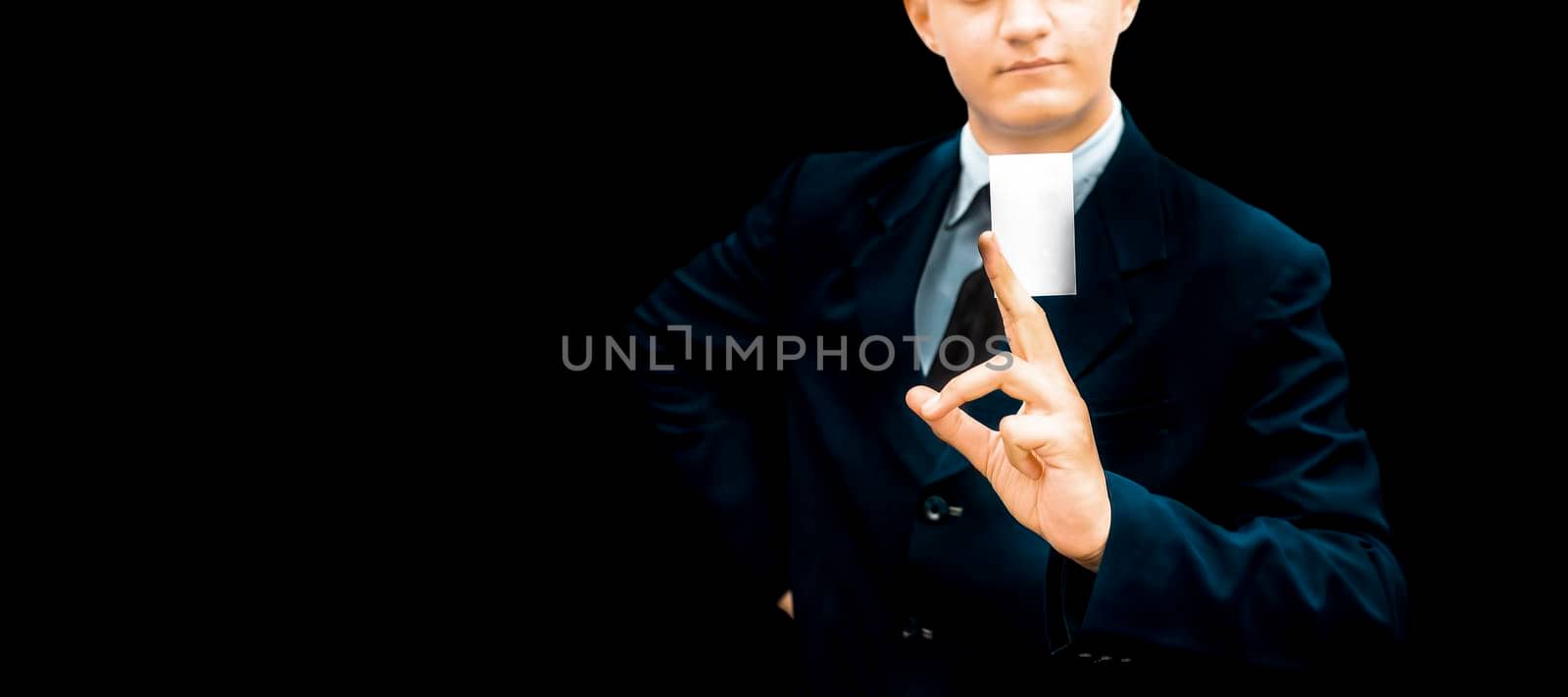 Unrecognizable gentleman or seller holding white colored card in his hand wearing a dark blue colored suit with black necktie isolated on black.Concept of marketting.