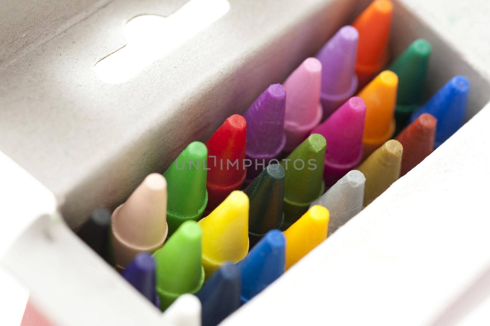Box full of colored wax crayons viewed from above with the lid open looking down on the tips in the colors of the spectrum in an art and creativity concept