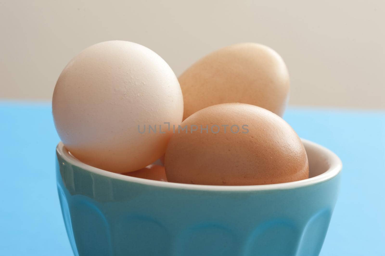 Fresh whole raw brown and white hens eggs in a blue ceramic bowl on a blue kitchen table in a close up view