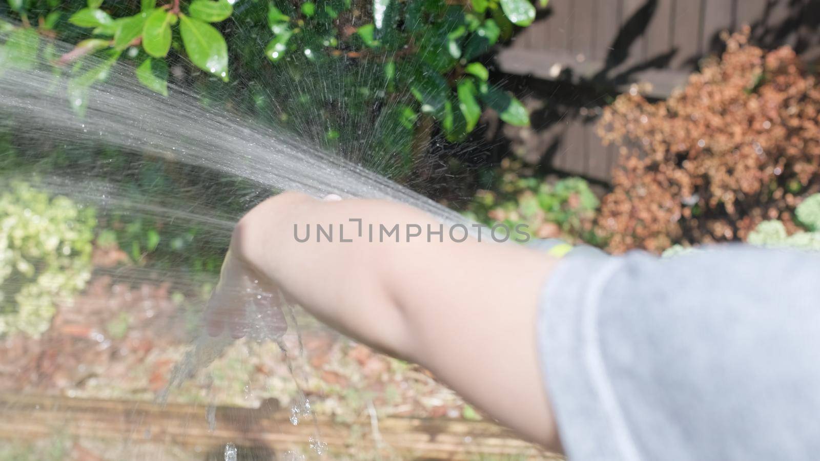 Funny little boy watering lawn plants in garden housing backyard. Adorable child playing with irrigation hose at hot sunny summer outdoors. Children help with housework. activity for kids. Childhood.