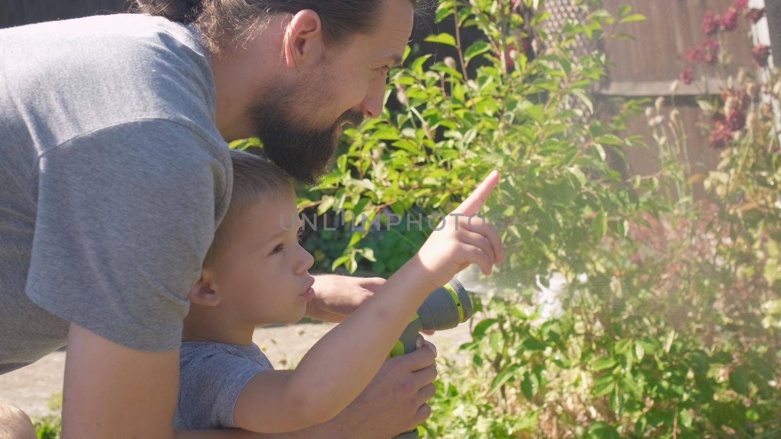 Father and Son. Funny little boy watering lawn plants in garden housing backyard with Dad. Summer house work. Hardworking preschool Kid outdoors. Children help with housework. activity for kids.