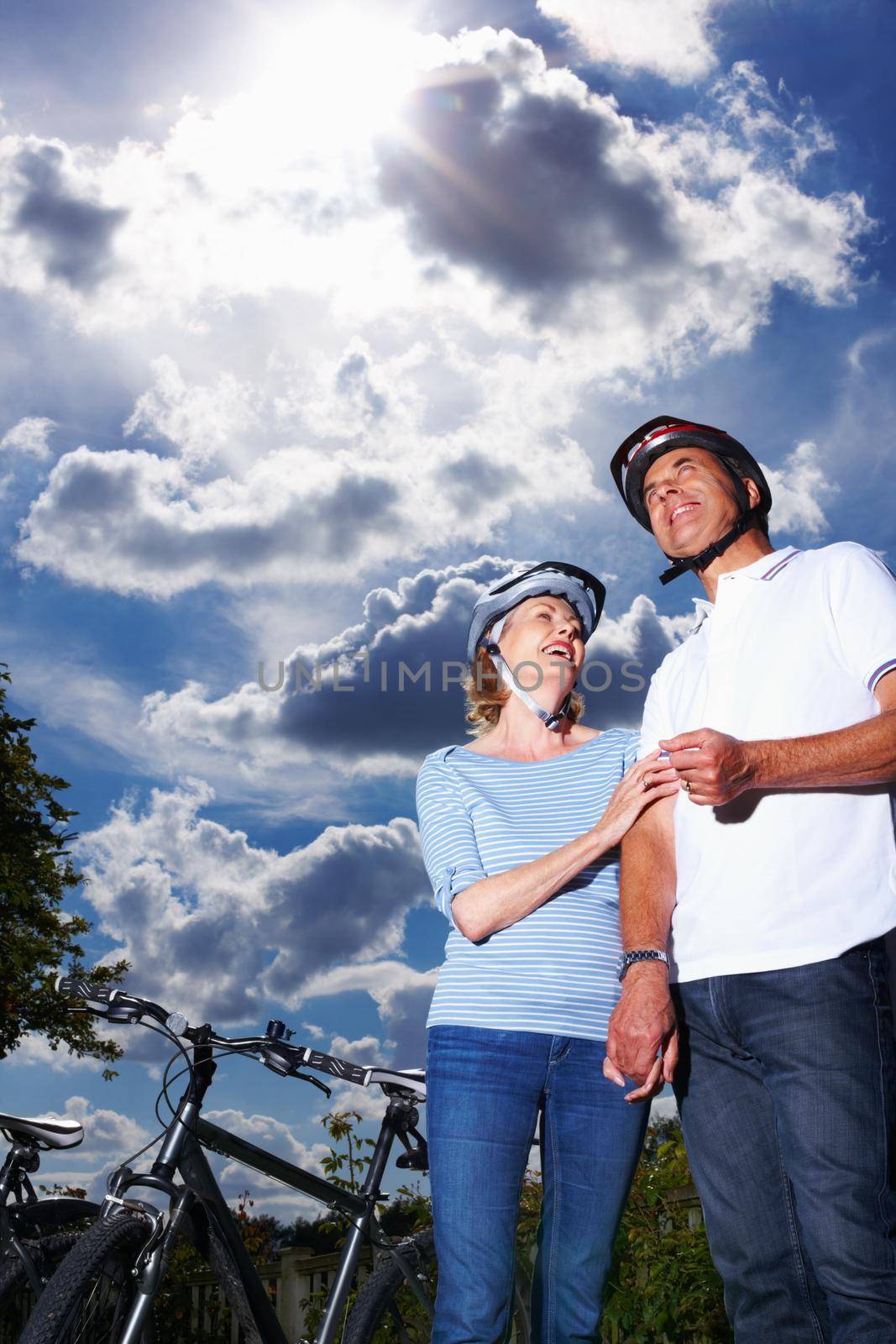 Romantic mature couple standing by bicycle against cloudy sky. Low section of romantic mature couple standing by bicycle against cloudy sky. by YuriArcurs