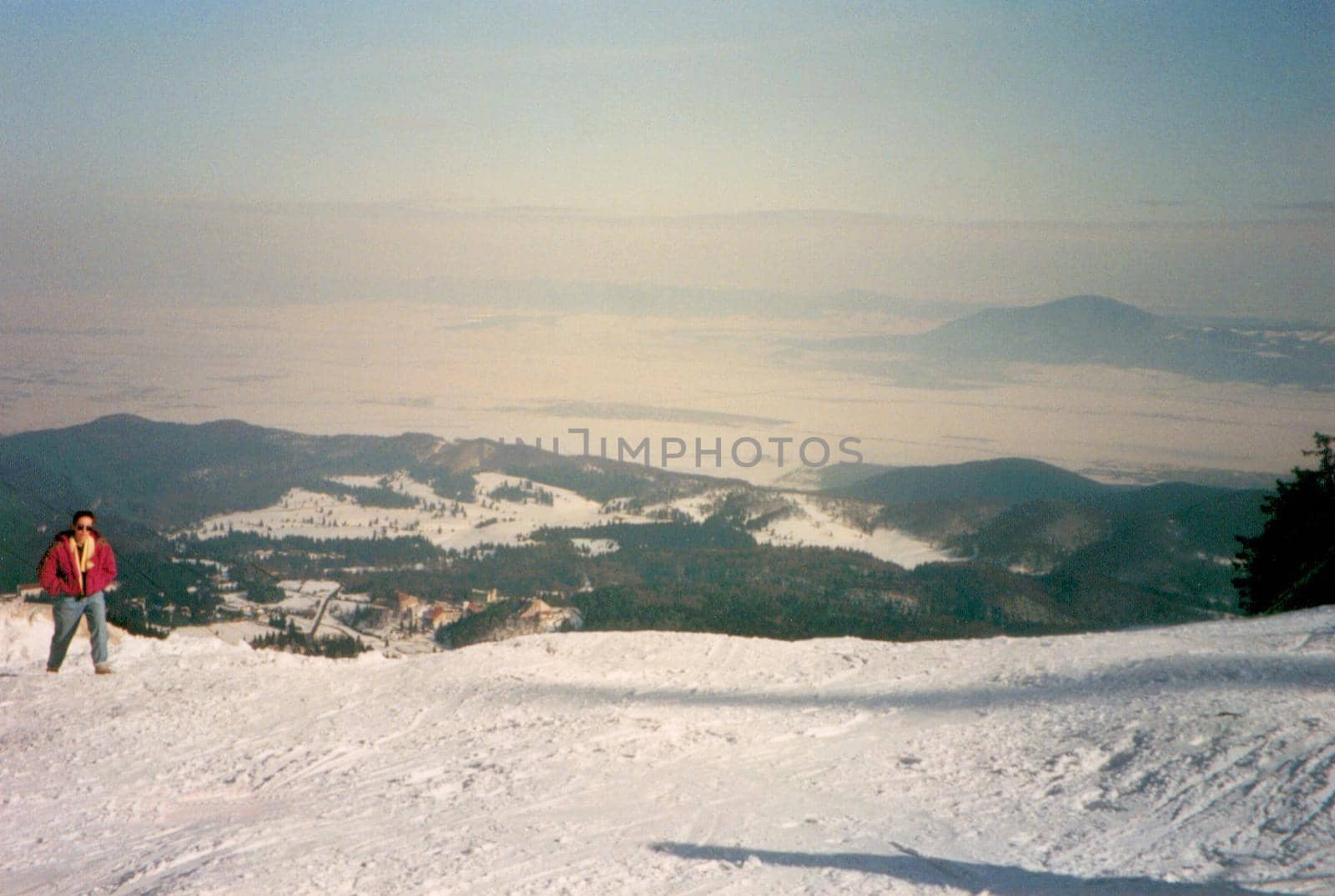 Man walking on a snow-capped mountain plateau or summit overlooking distant snowy mountain ranges on a sunny winter day