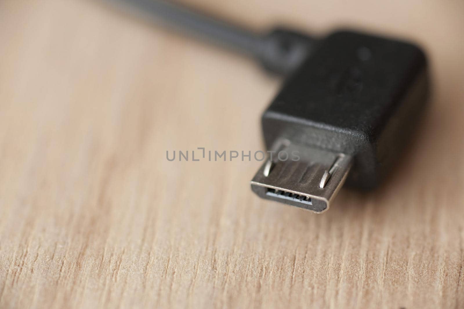Micro USB connector with black wire, close-up macro shot on wooden table with copy space