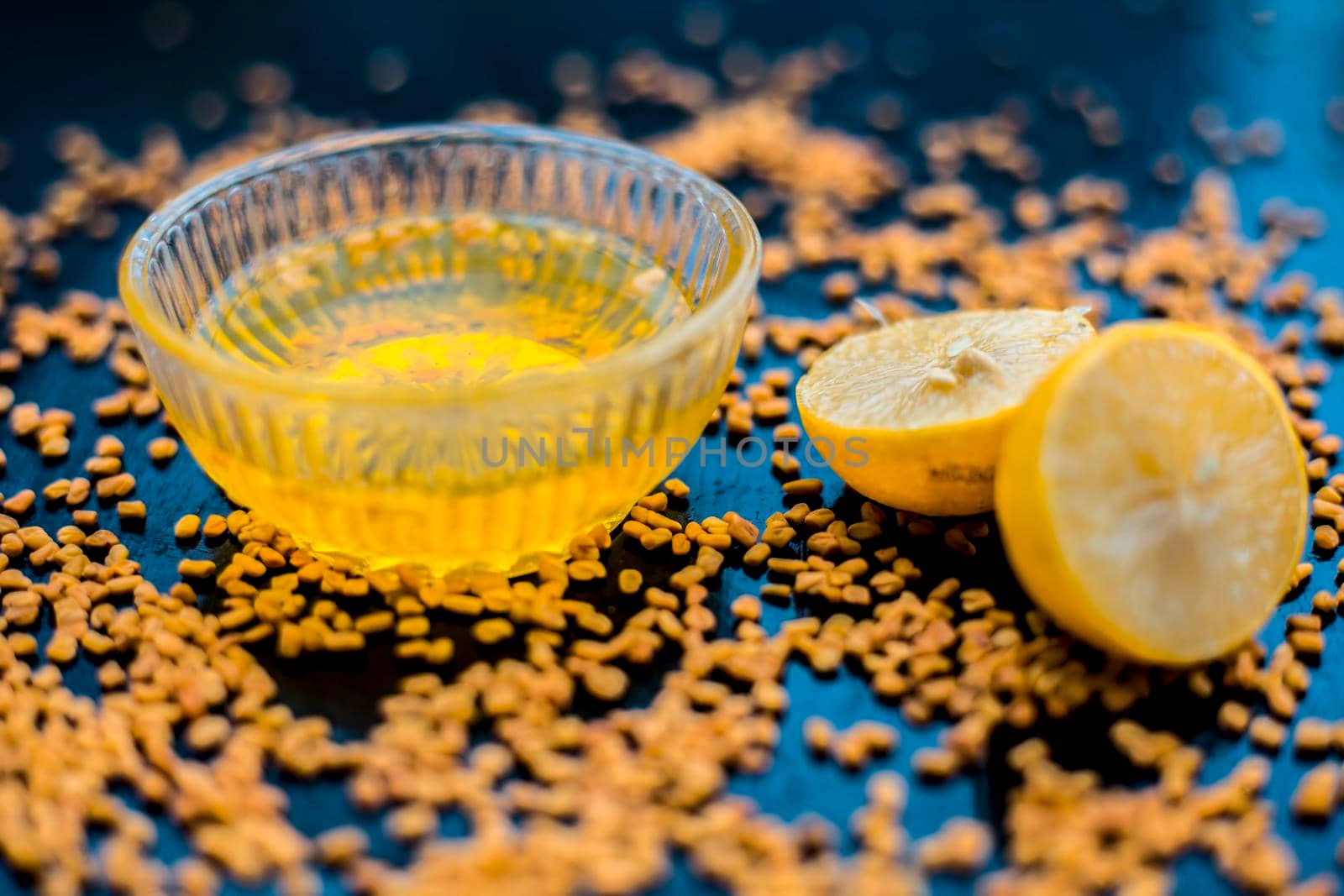 Famous natural method for dandruff on wooden surface in a glass bowl consisting of fenugreek seeds powder well mixed with lemon juice.With raw lemons and fenugreek seeds on the present on the surface.