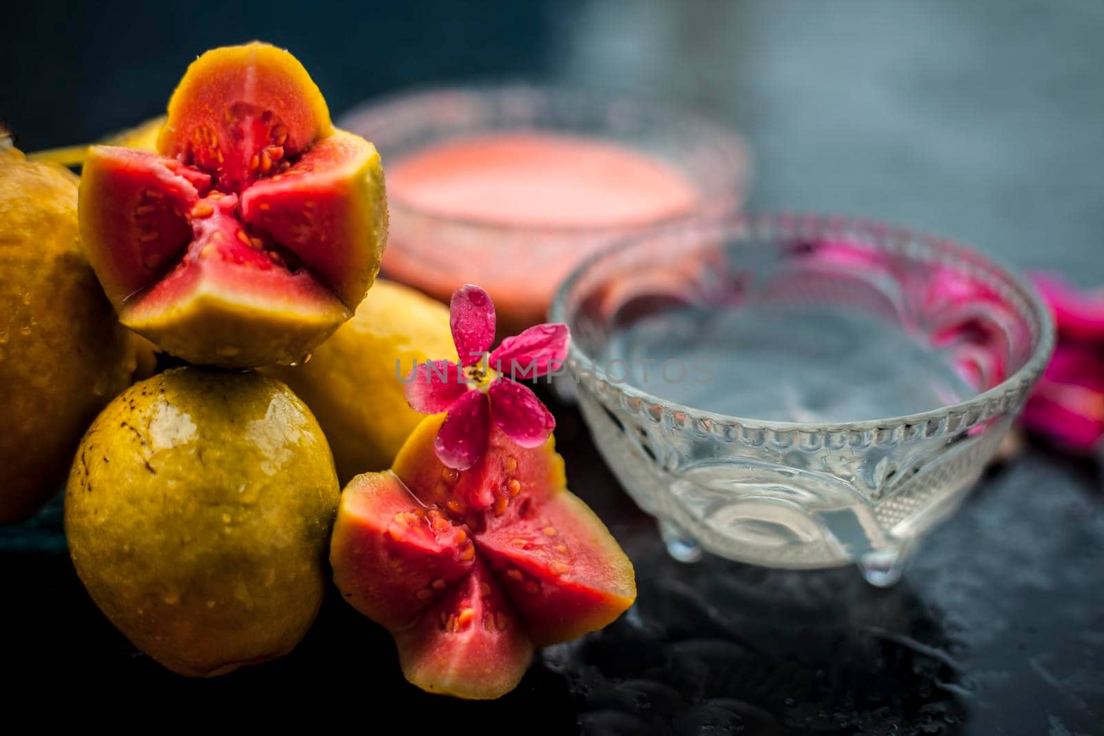 Guava pulp and water well mixed in a glass bowl on the wooden surface along with some raw cut guava, with some rose petals, also completing a face mask used for a natural glow.