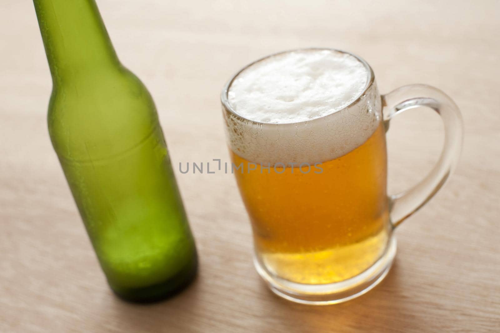 Close up high angle view of a glass tankard and unlabelled green bottle of cold beer on a wooden bar counter