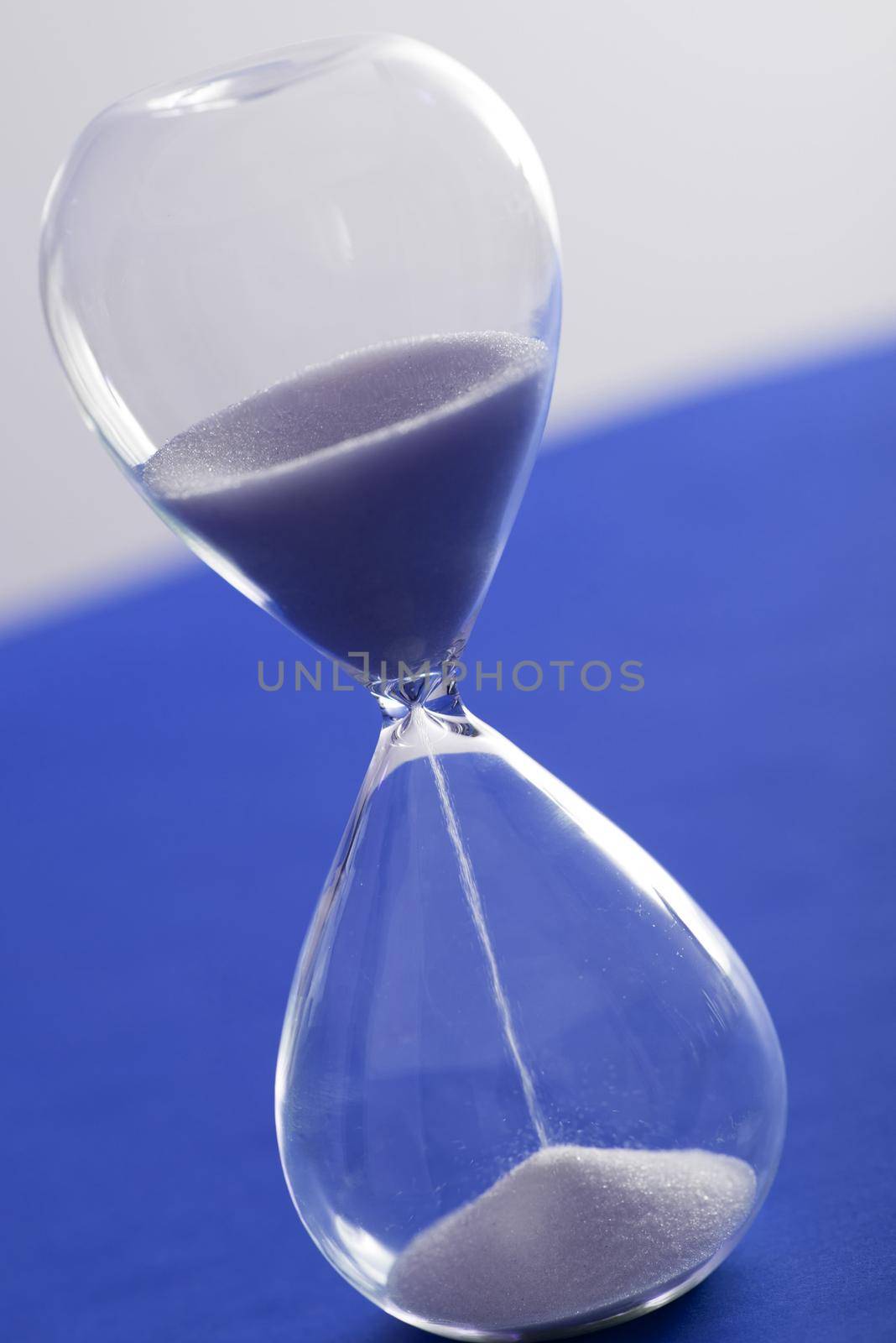 Tilted angle view of sand running through an hourglass over a blue and grey background measuring the passage of time