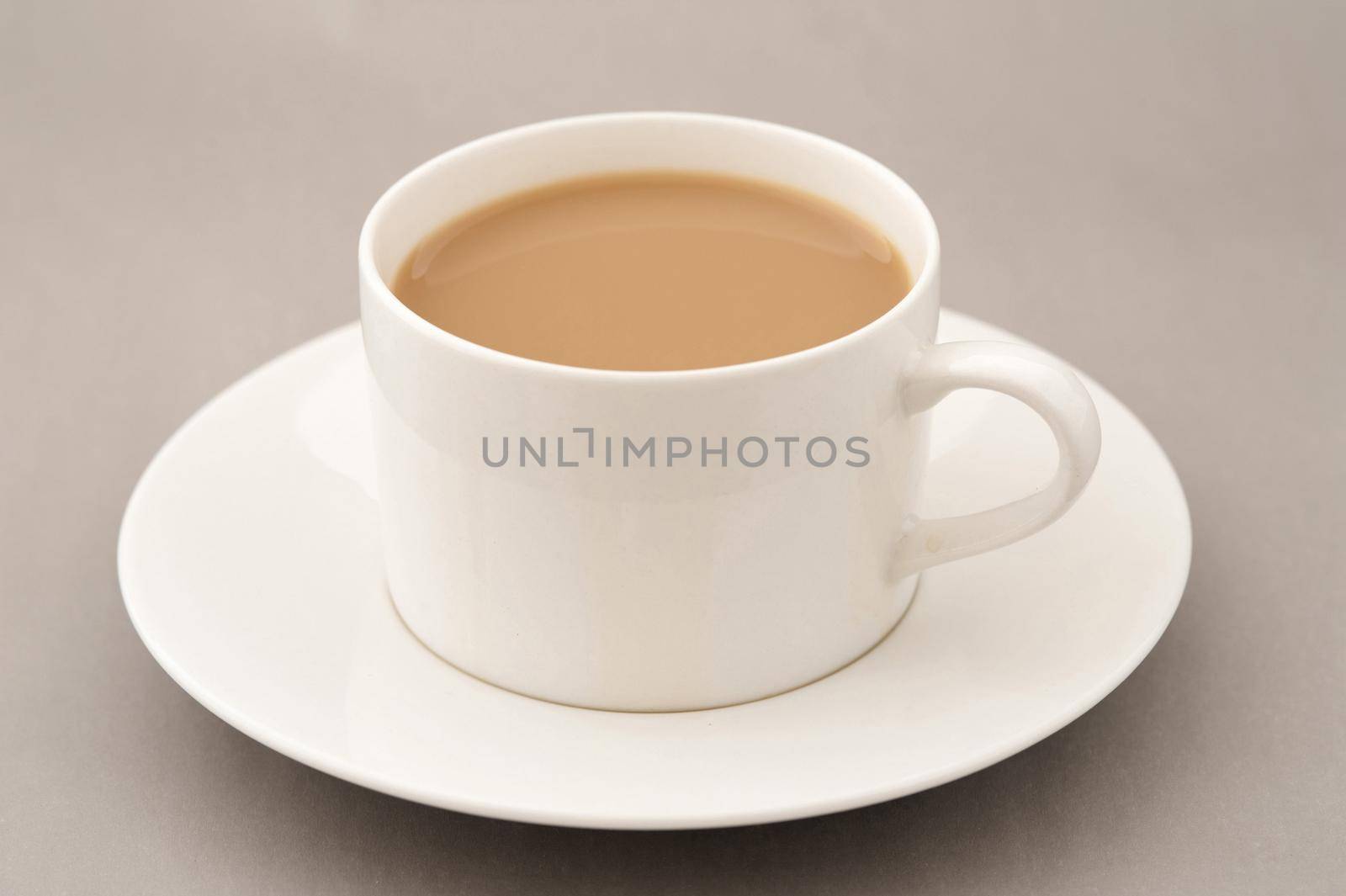 Cup of coffee with milk on saucer standing on grey table