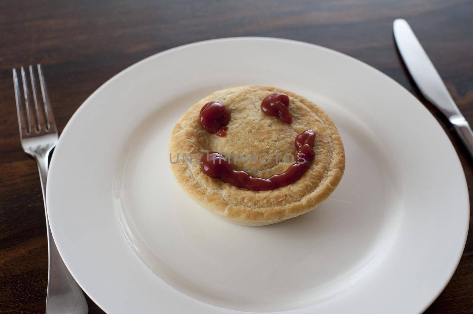 Meat pie with a smiley gravy face on the crusty pastry served on a plate for a lunchtime snack