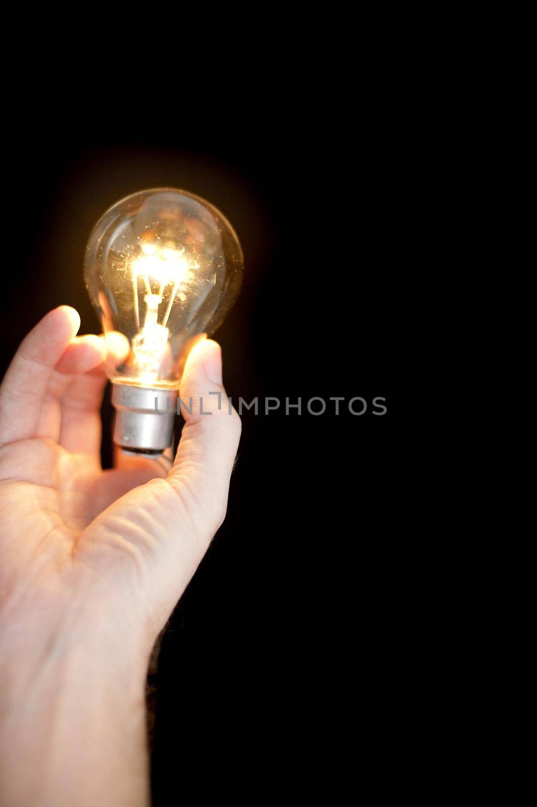 a hand holding a glowing lightbulb with space for copy on a black background