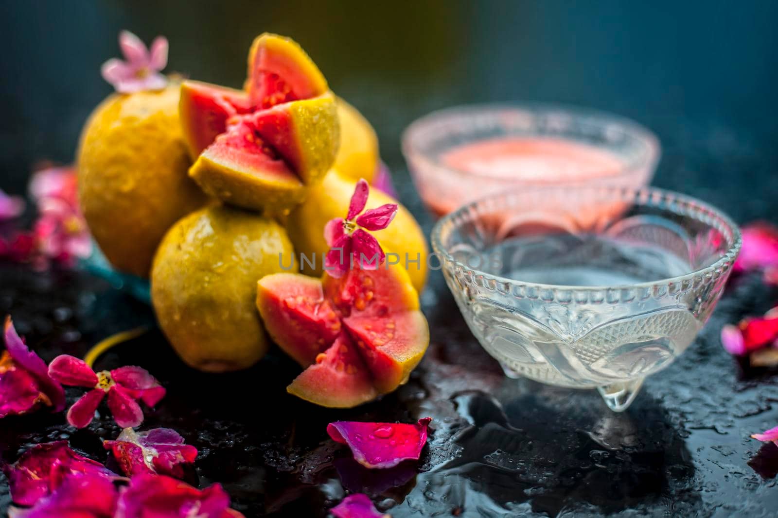 Guava pulp and water well mixed in a glass bowl on the wooden surface along with some raw cut guava, with some rose petals, also completing a face mask used for a natural glow. by mirzamlk