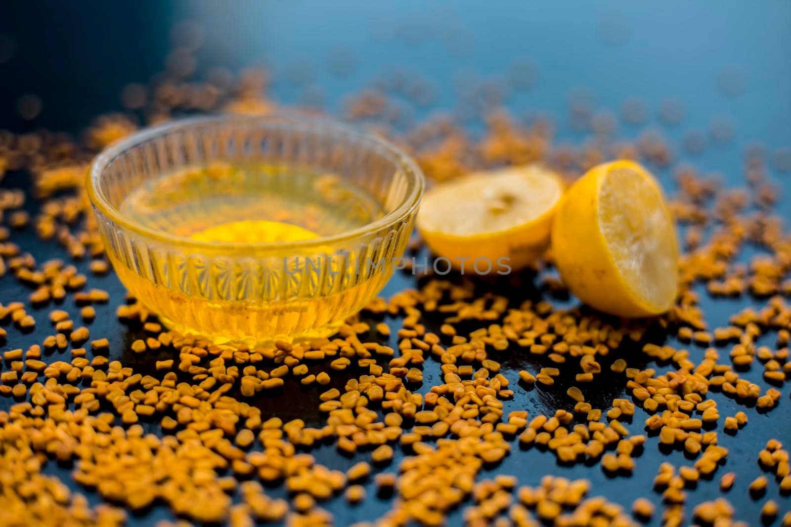 Famous natural method for dandruff on wooden surface in a glass bowl consisting of fenugreek seeds powder well mixed with lemon juice.With raw lemons and fenugreek seeds on the present on the surface.