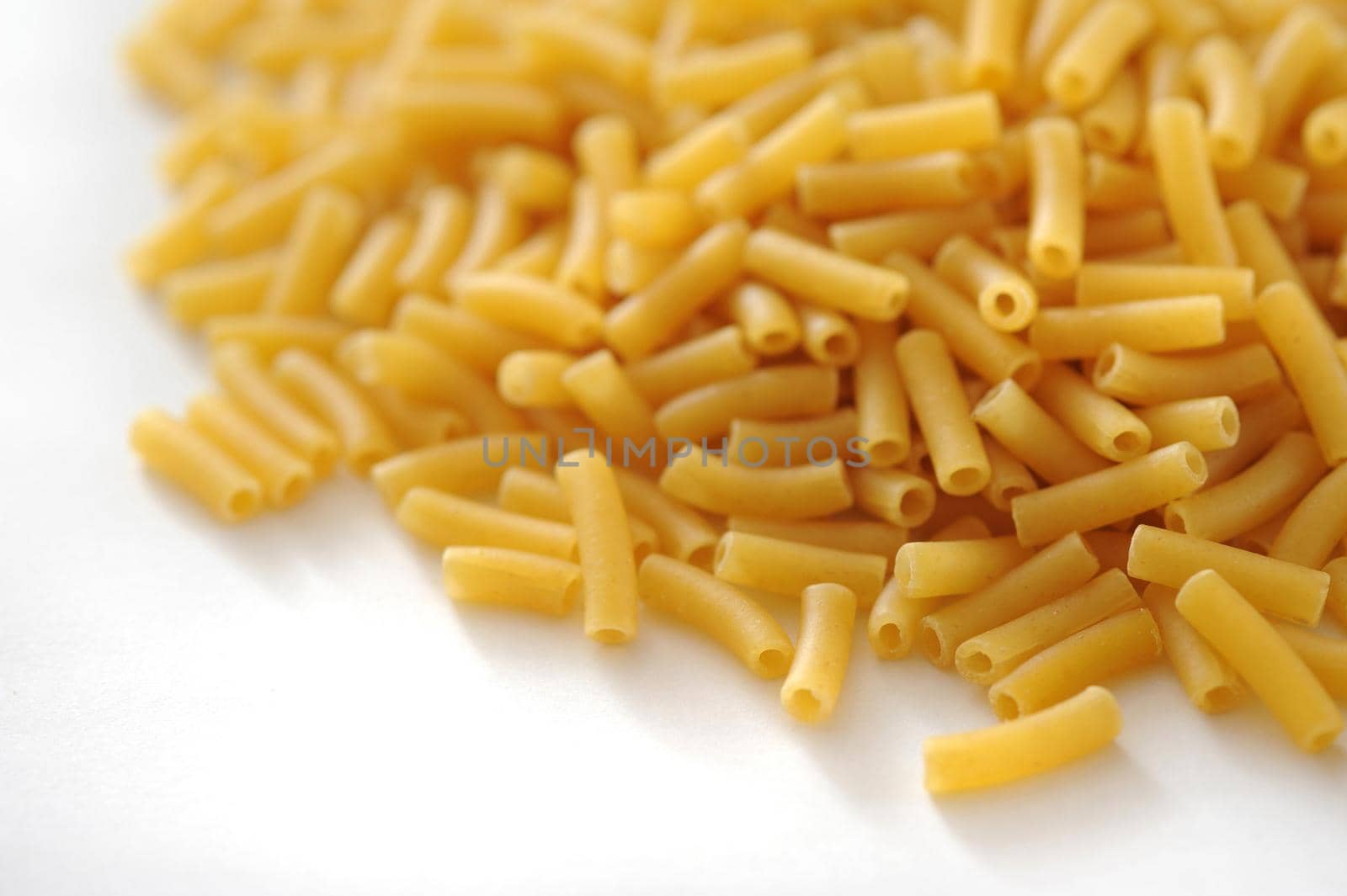 Heap of dried macaroni pasta for Italian and Mediterranean cooking on a white background with copyspace