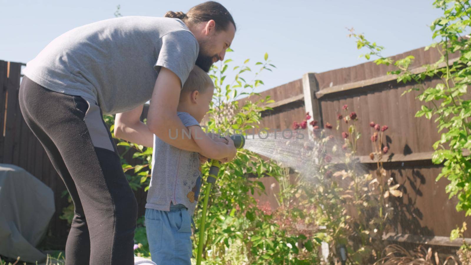Father and Son. Funny little boy watering lawn plants in garden housing backyard with Dad. Summer house work. Hardworking preschool Kid outdoors. Children help with housework. activity for kids by mytrykau