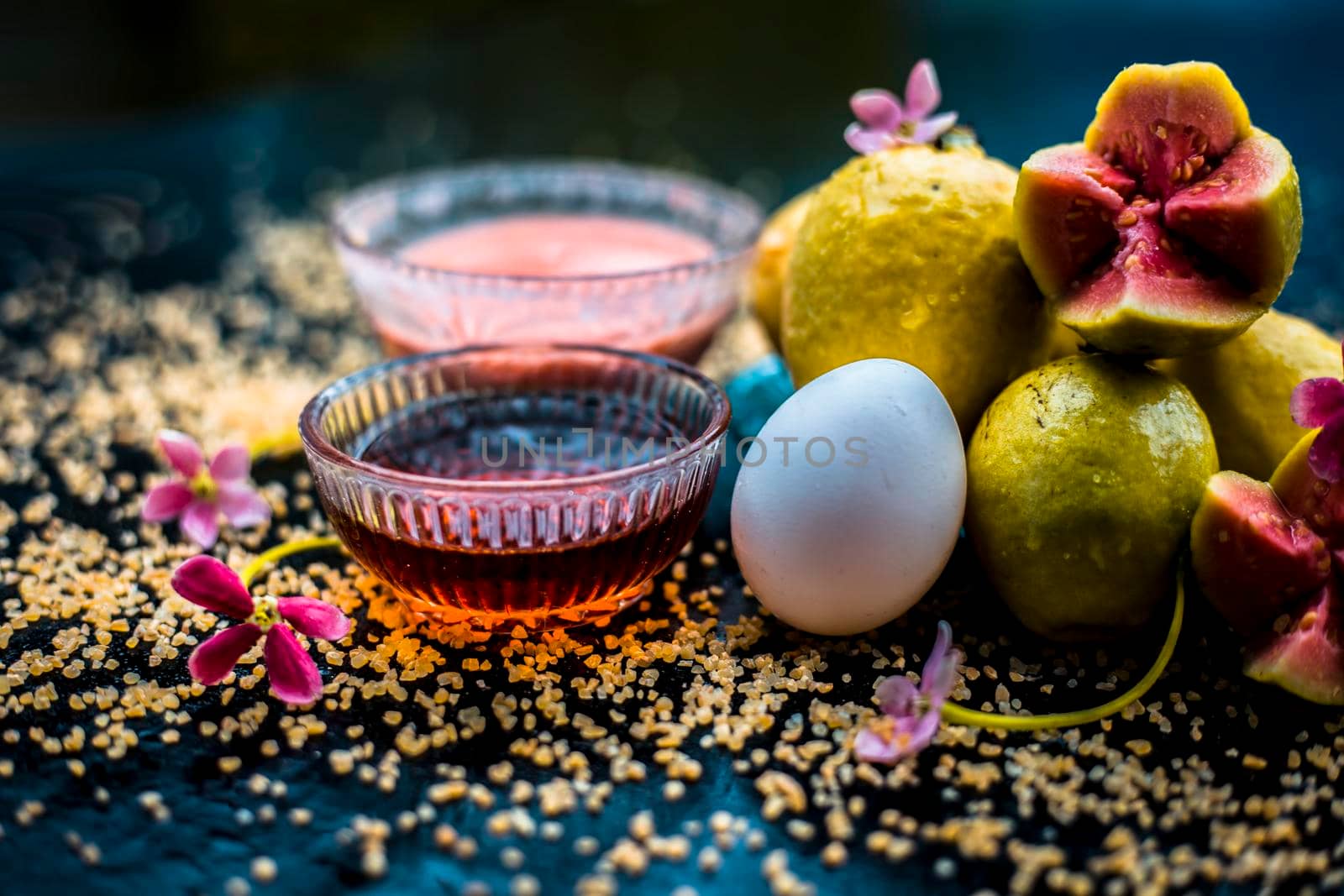 Treatment of dry skin with the help of face mask on a wooden surface consisting of honey, guava pulp, egg yolk, and some oatmeal, well mixed in a glass bowl along with raw ingredients.