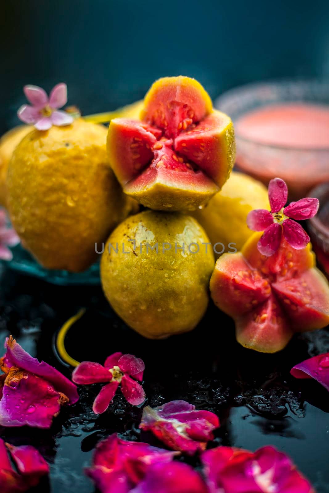 Raw organic guava or amrut or amarood in Hindi language on black shinny surface in a blue-colored plate with some rose petals. by mirzamlk