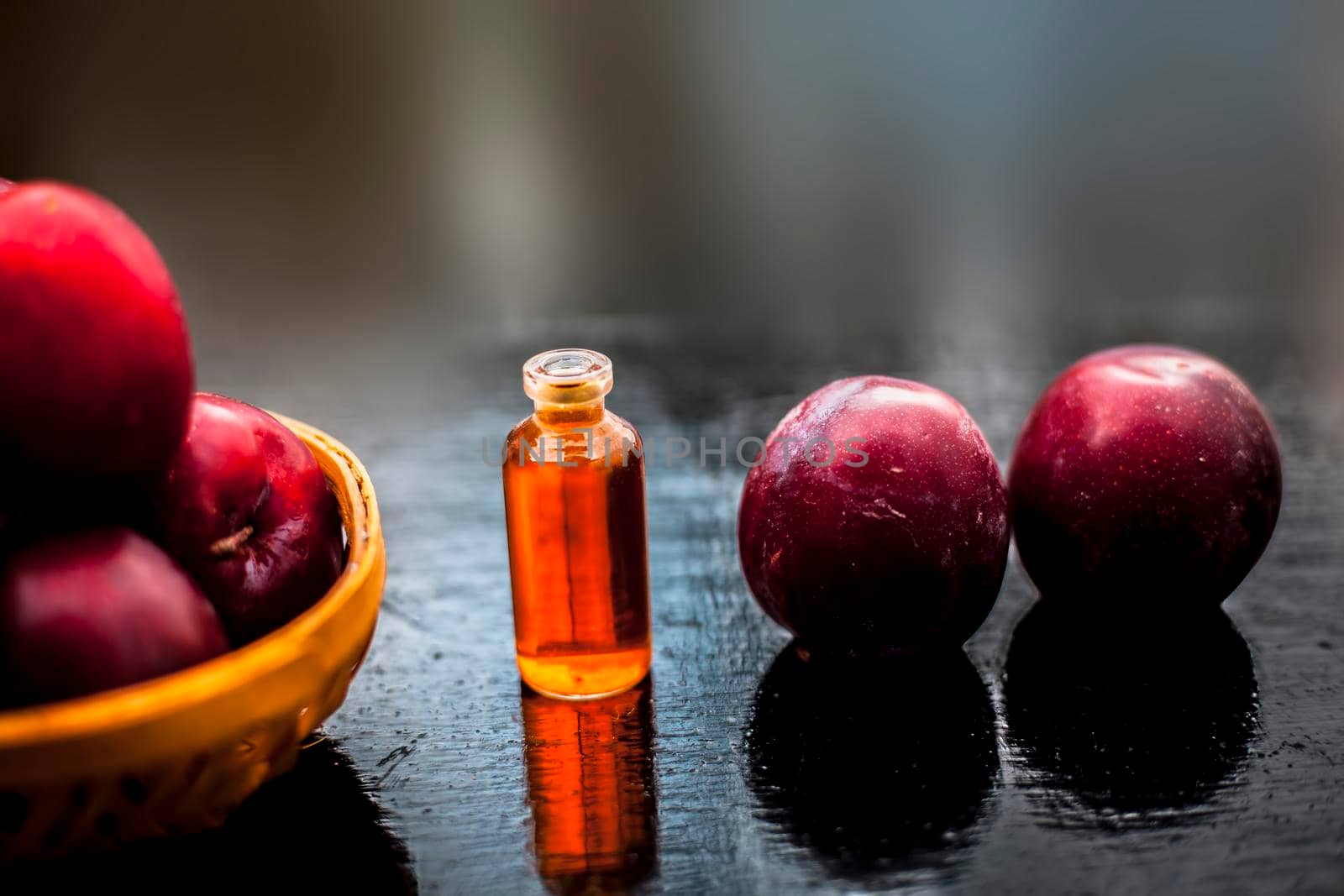 Raw ripe red plums along with its extracted essential concentration or essence in a glass bottle on a wooden surface.