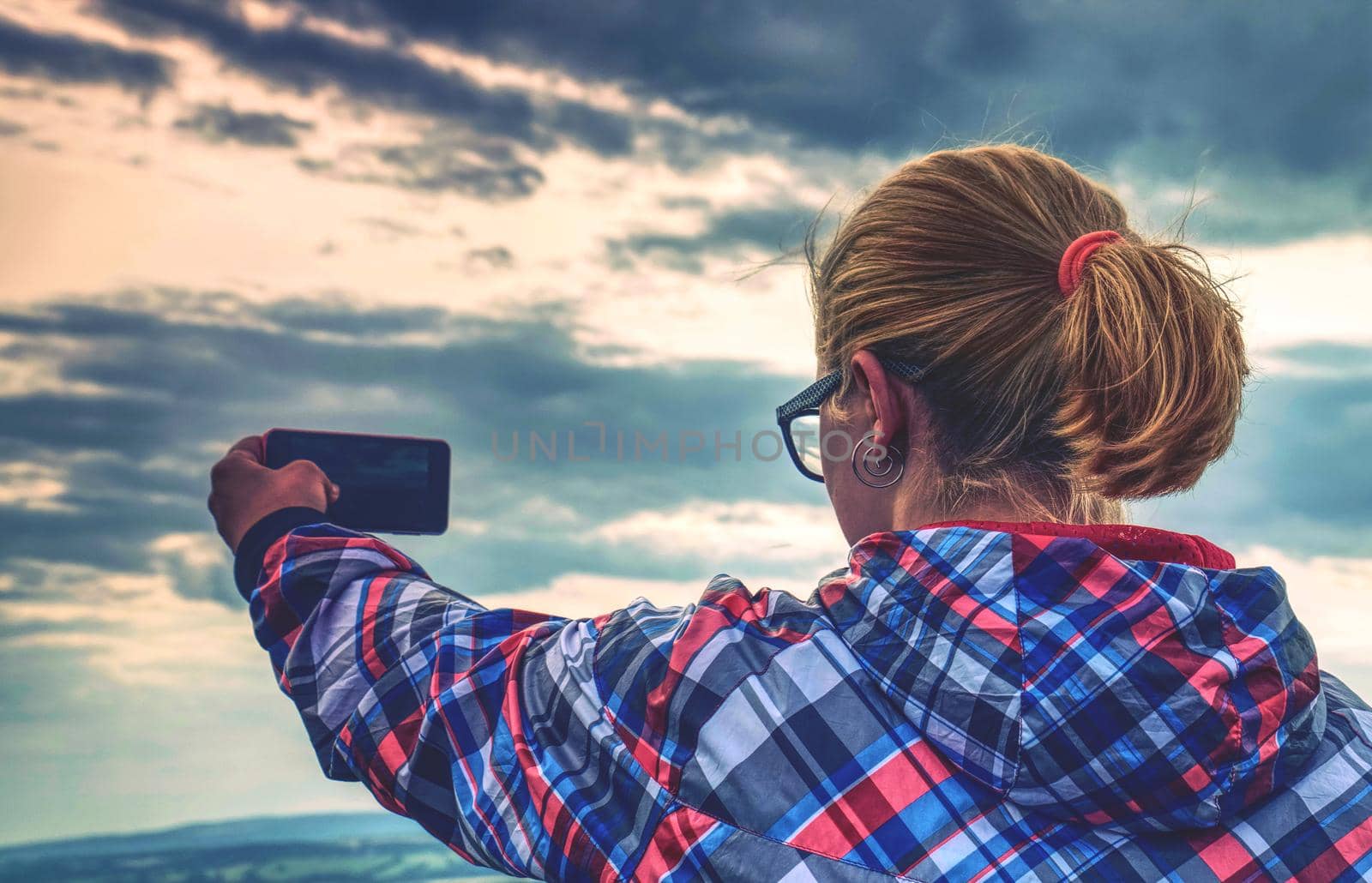 Successful female hiker taking photo on cliff edge. Cute girl on  rock making a photo on a smartphone.