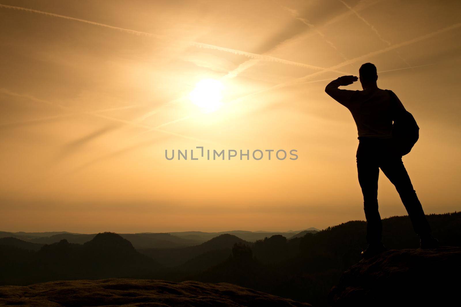 Man shadowing eyes. Alone tourist on cliff edge and watching into deep valley bellow. Fall weather. by rdonar2