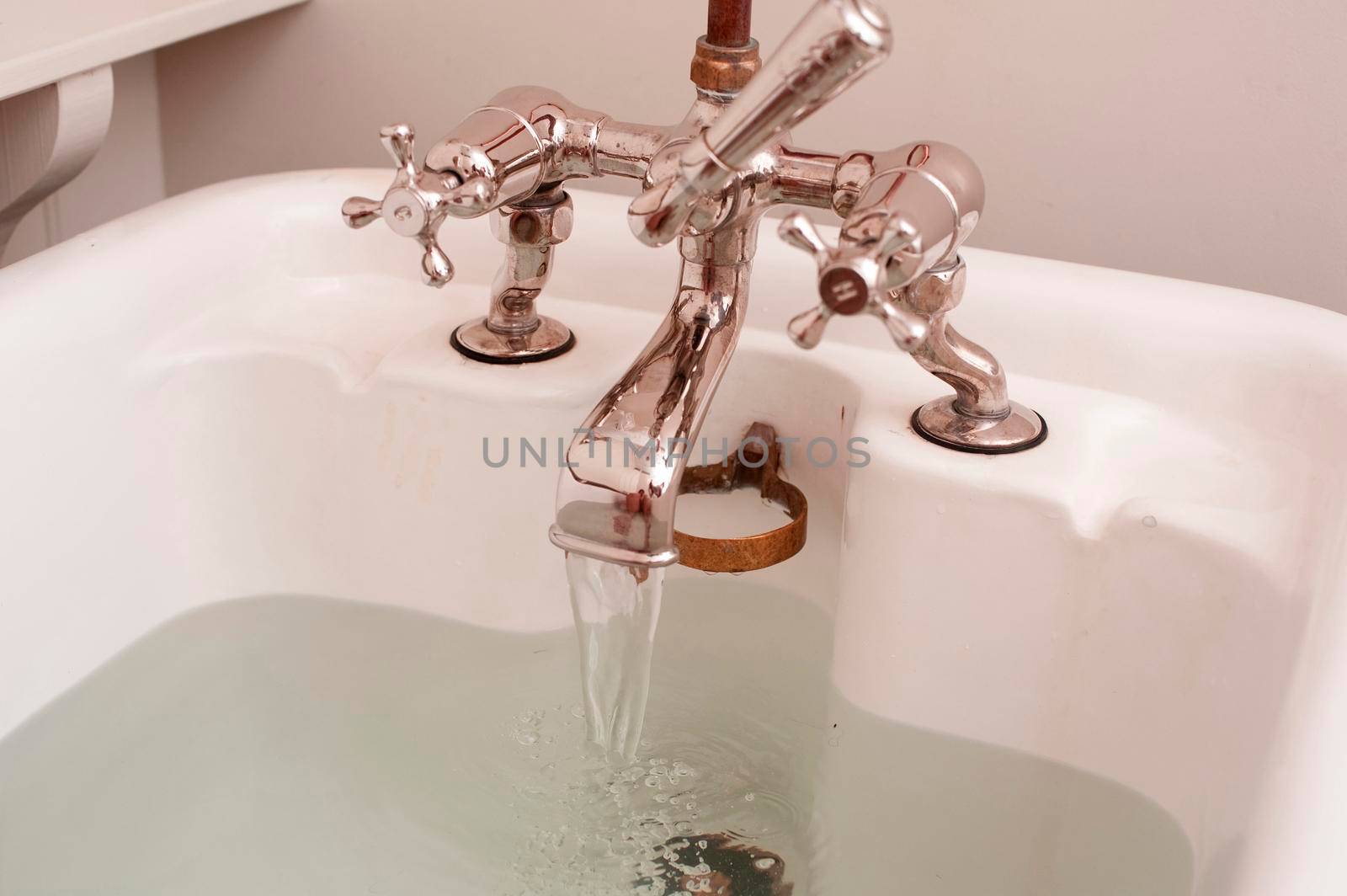 Partial view of a bathtub with running water from an old-fashioned faucet