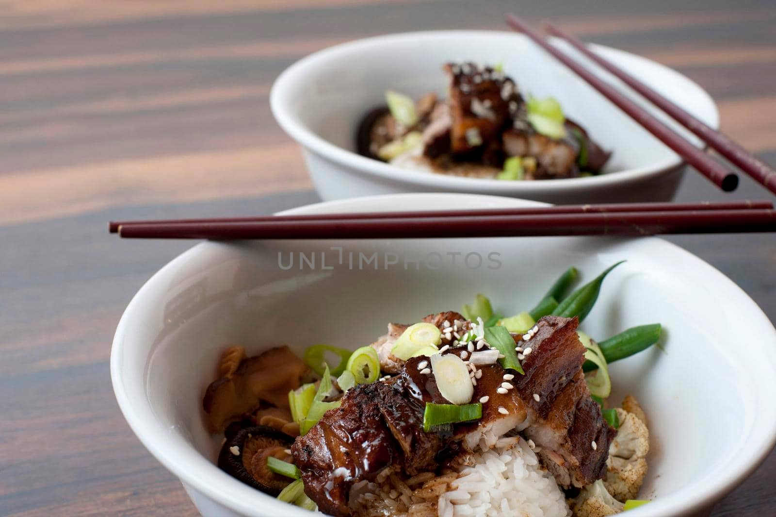 Close up of a bowl of Chinese fatty pork and vegetables topped with a rich sauce and served with chopsticks
