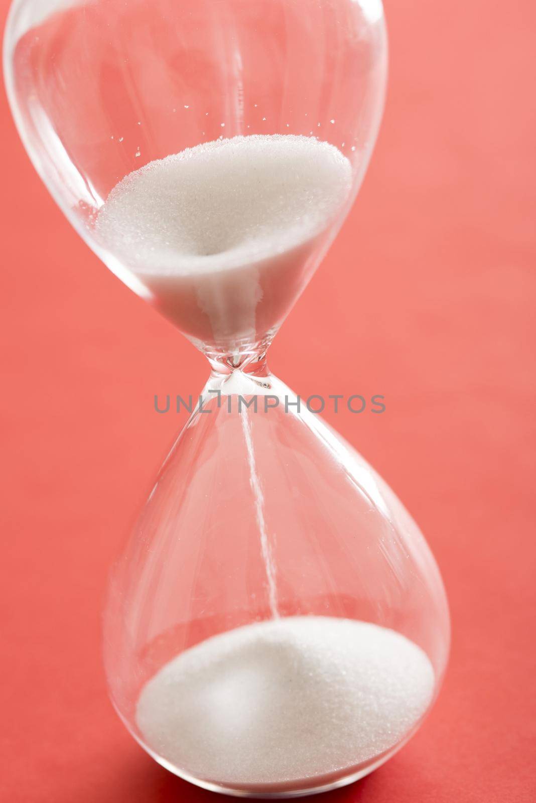 White sand running through an hourglass or egg timer measuring passing time counting down to the end or a deadline over a red background