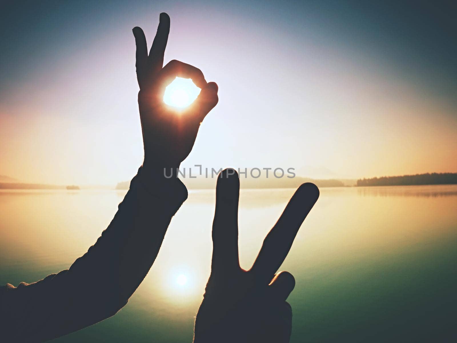 Hand touch Sun.  Palm shadow play with rising sun above lake and sun rays. Funny happy concept.