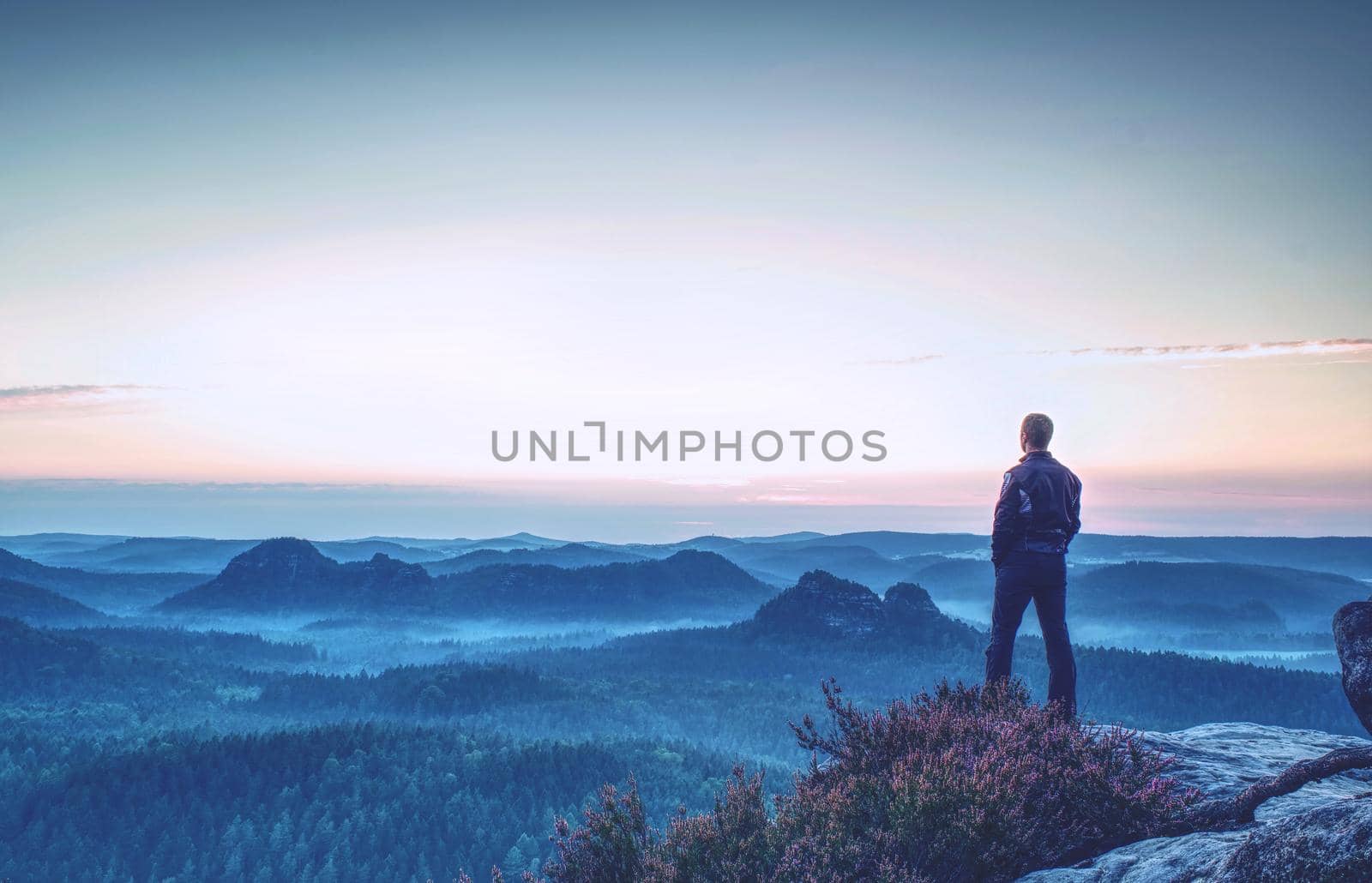 Hiker stands and enjoys valley view from hilly viewpoint. Hiker reached top of the mountain and watching sunset.