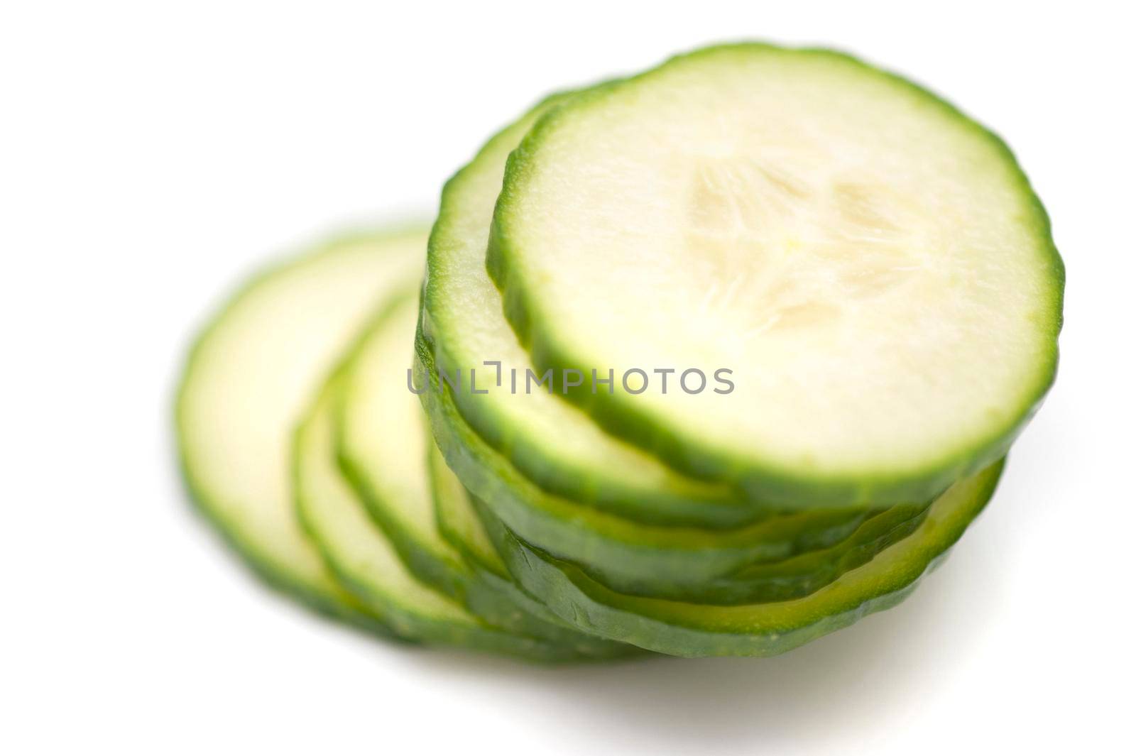 Stacked sliced cucumber with focus to the top slice showing the fleshy pulp and green rind on white