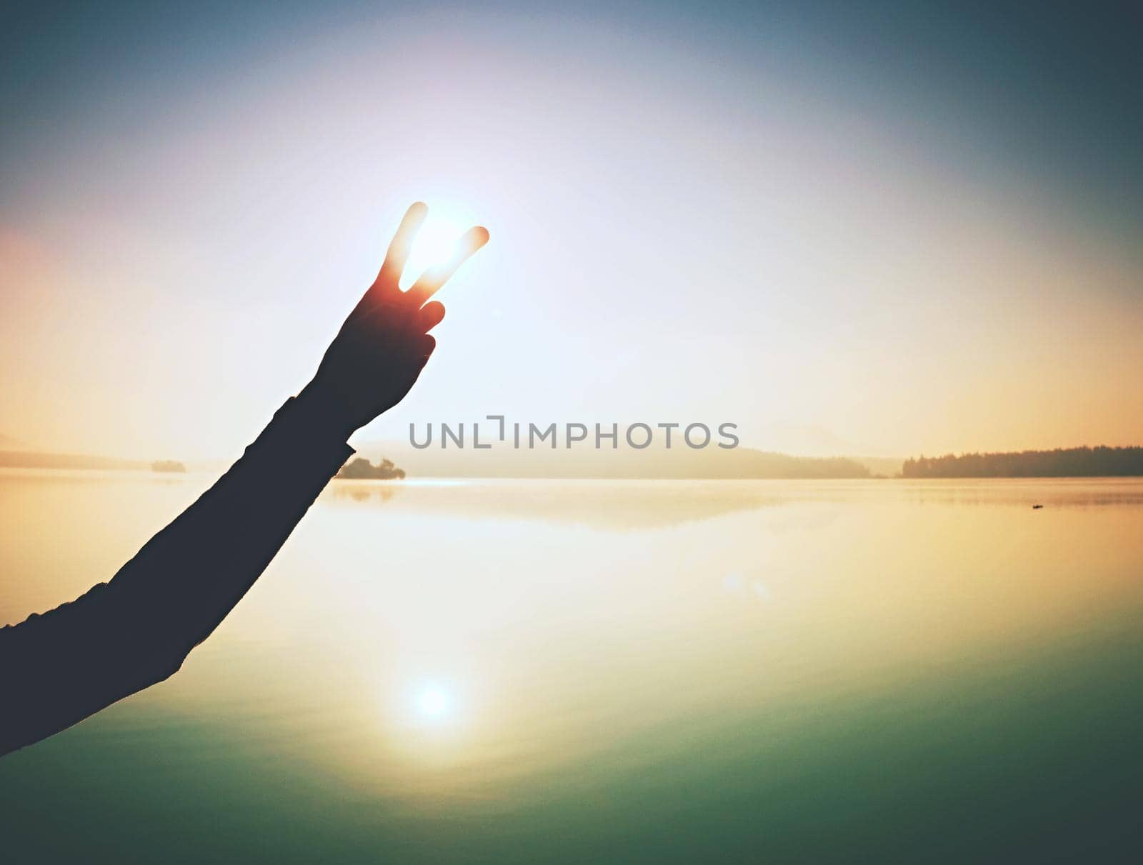Hand touch Sun.  Palm shadow play with rising sun above lake  by rdonar2