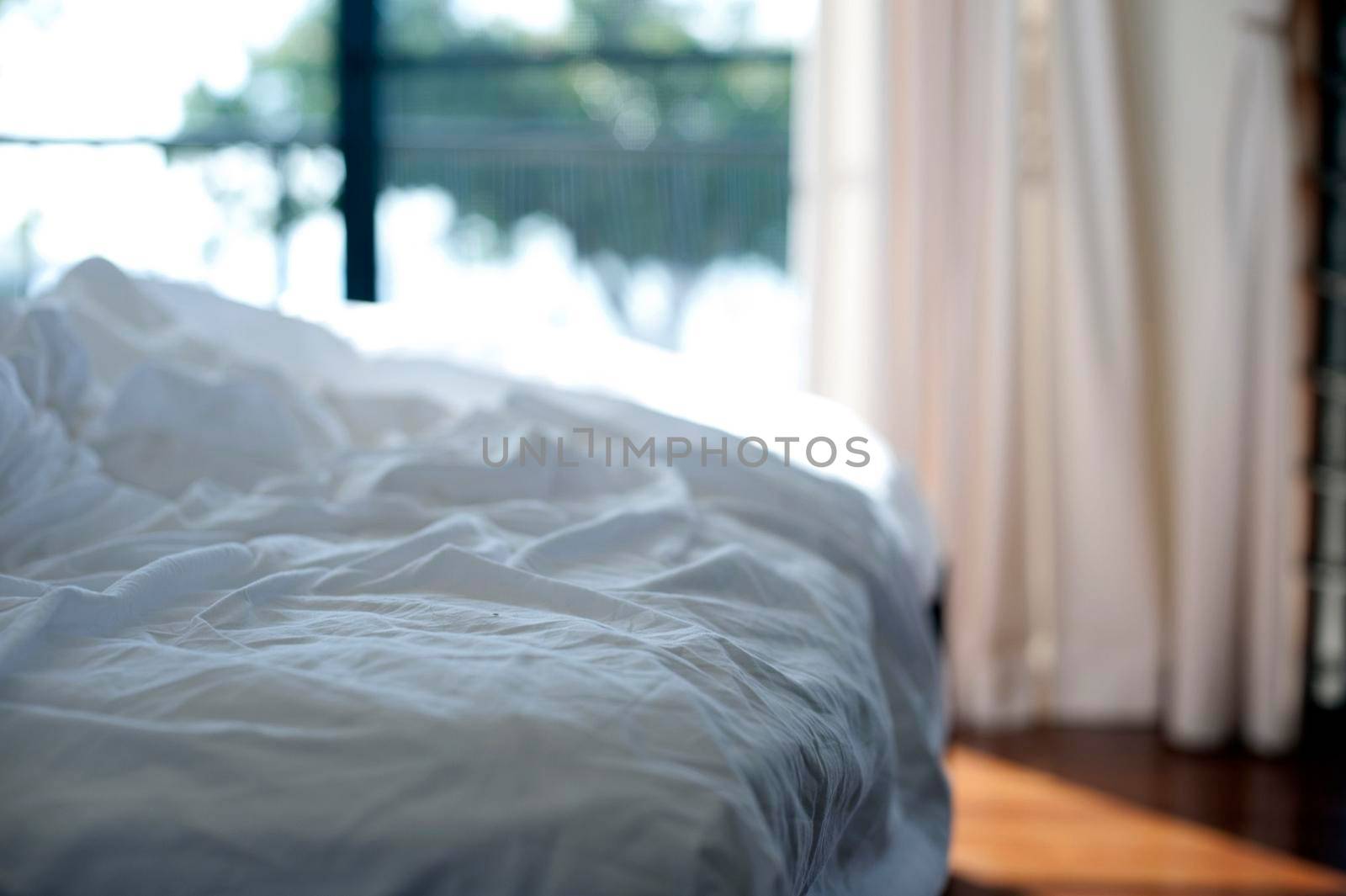 Empty messy unmade bed with white bed linen and crumpled sheets, close up view in front of a bright window