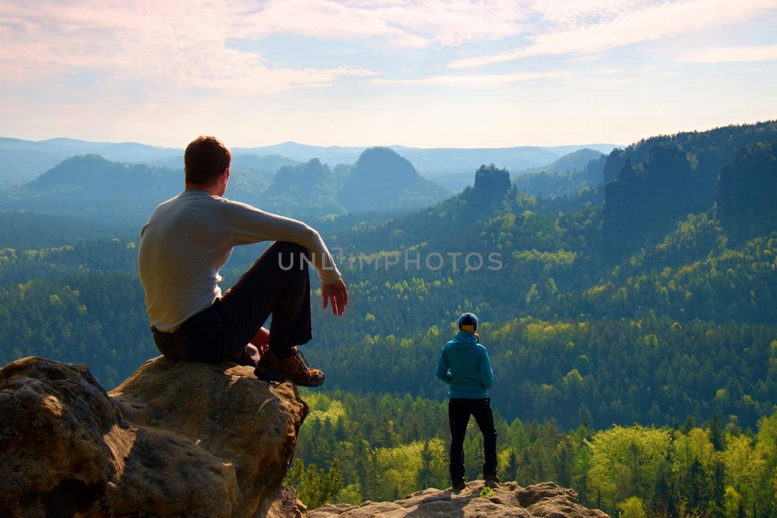 Boy and girl  tourists  stay on cliff and thinking. Dreamy fogy landscape, blue misty sunrise in beautiful valley below by rdonar2