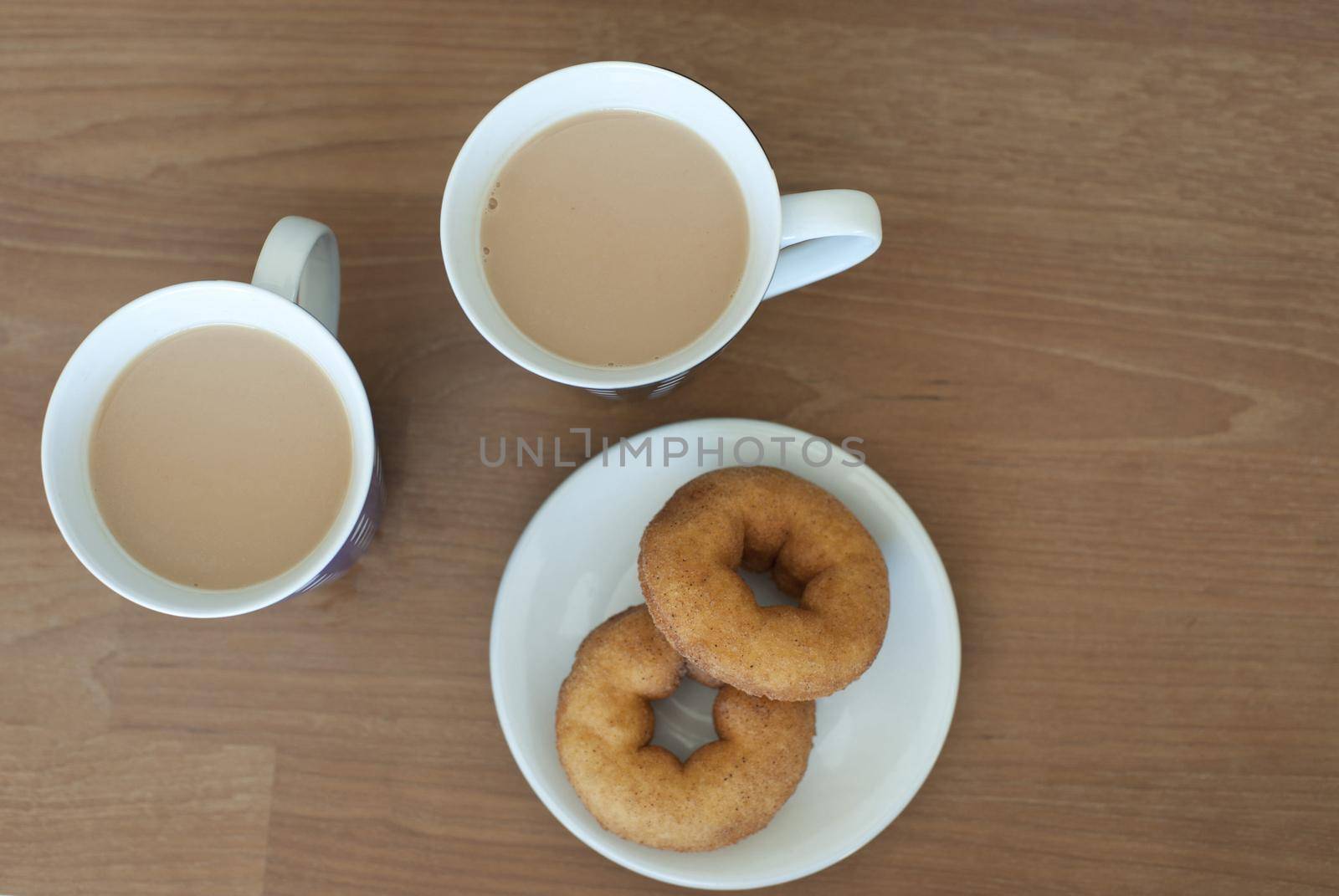 Aerial View of Cups of Creamy Coffee and Plate of Doughnuts on Side Served on Brown Wooden Table