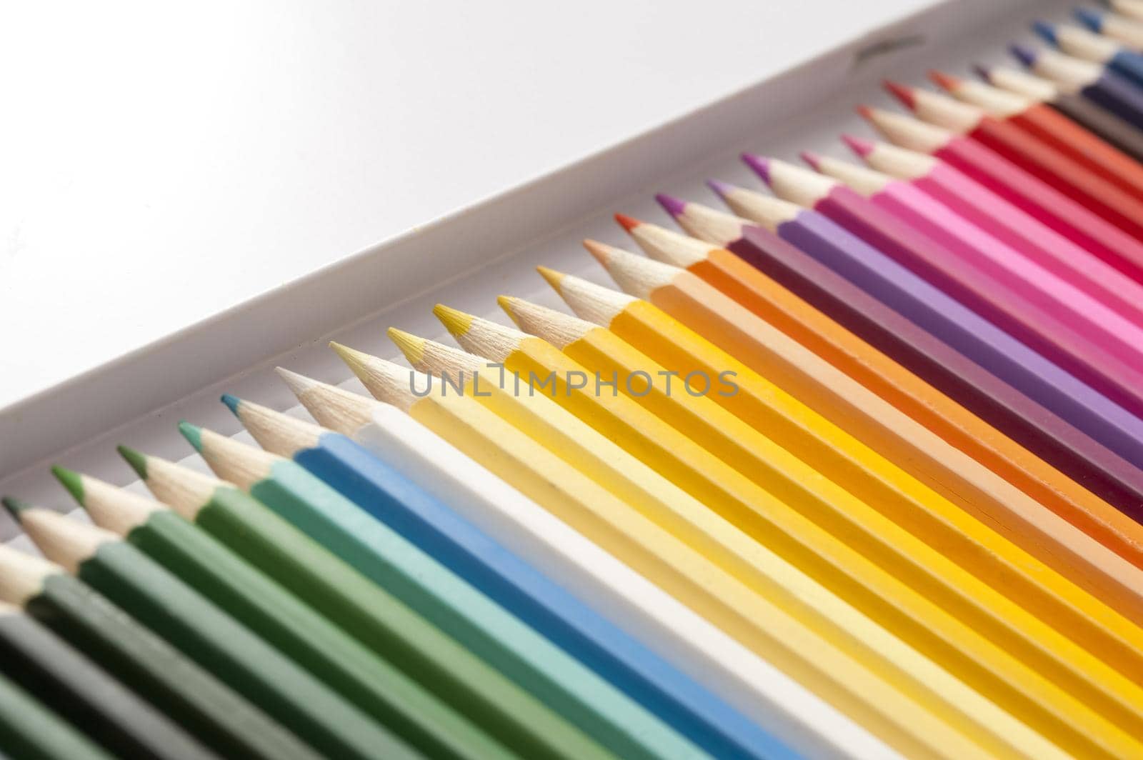 Open box of newly sharpened pencils in dark and bright colors arranged in a long row with selective focus