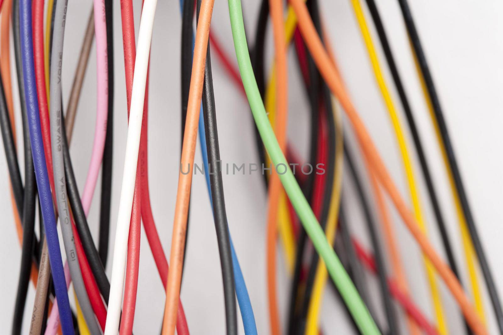 Jumble of colorful electric wires with plastic covering in the colors of the rainbow over a white background in an electronics and technology concept