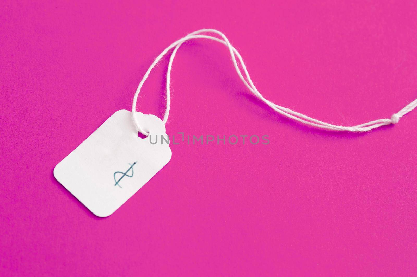 White cardboard price label or tag with string and a handwritten dollar sign lying on a bright pink background with copy space
